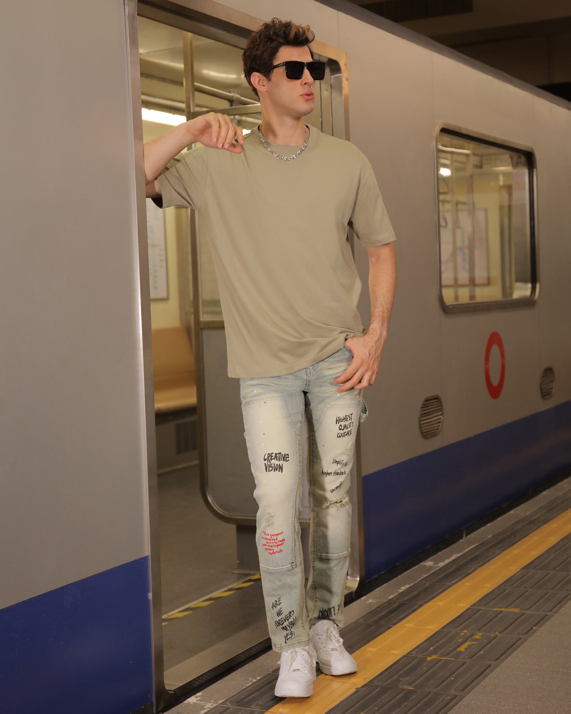 Man wearing Logeqi spray paint graffiti jeans with white sneakers standing in subway train doorway