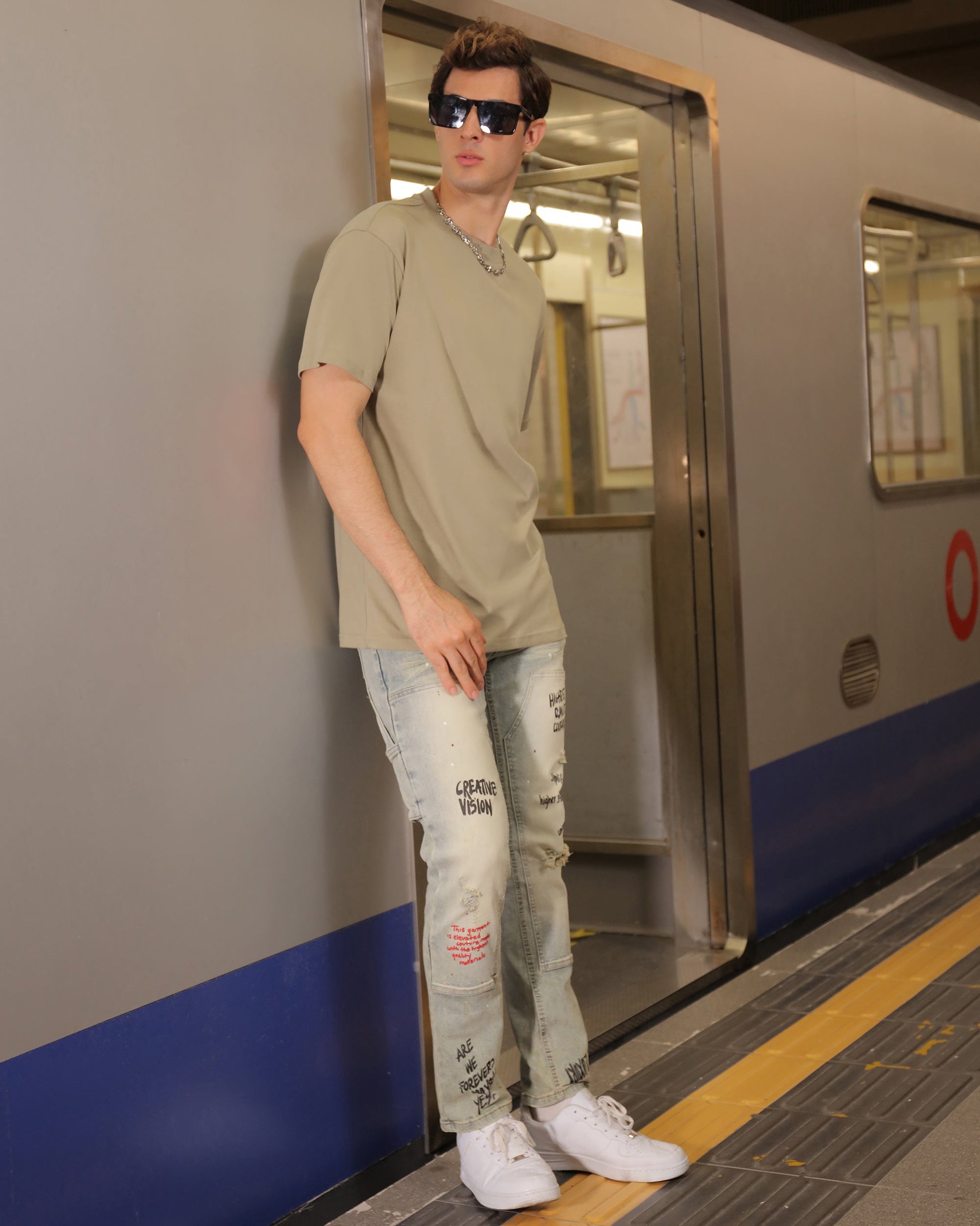Logeqi spray paint graffiti jeans worn by man standing at subway train entrance in casual outfit