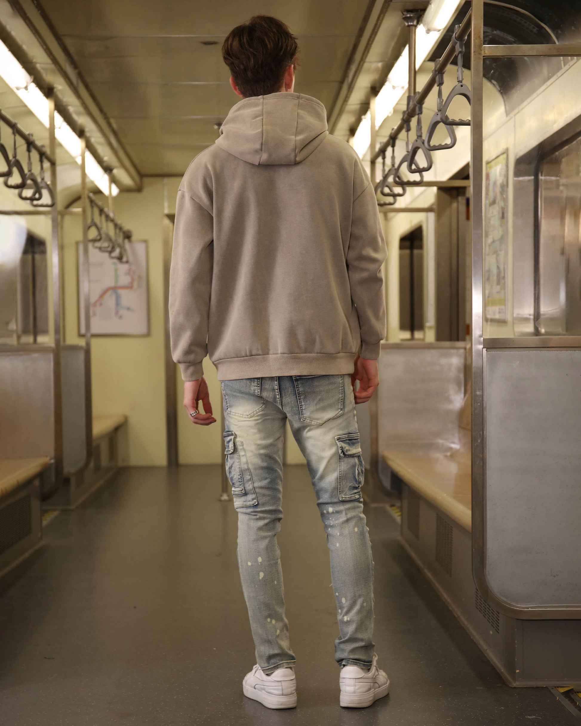 Logeqi spray painted blue cargo jeans worn by a man standing in a subway train with a gray hoodie and white sneakers