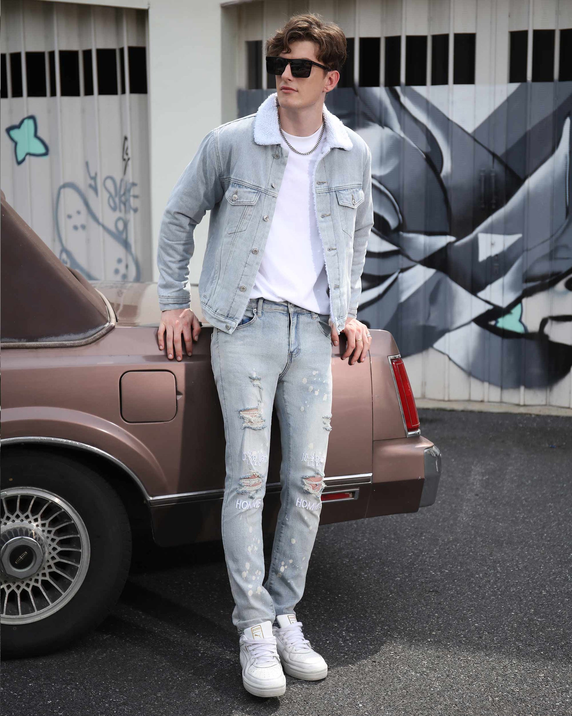 Logeqi spray painted light blue ripped jeans worn by man standing next to vintage car in urban setting