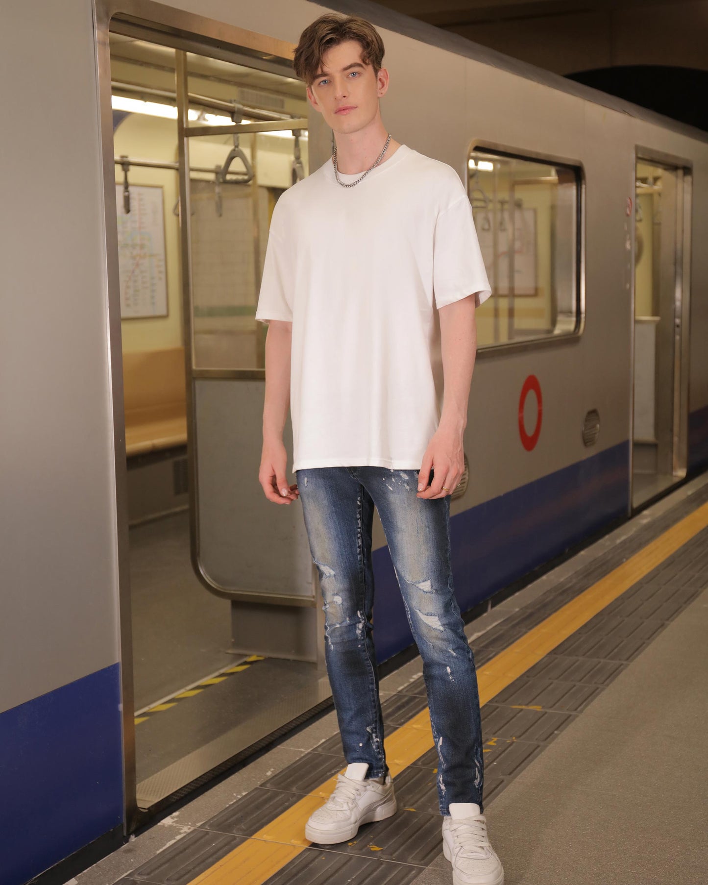 Man wearing Logeqi unique blue wash jeans with white t-shirt and sneakers standing by subway train