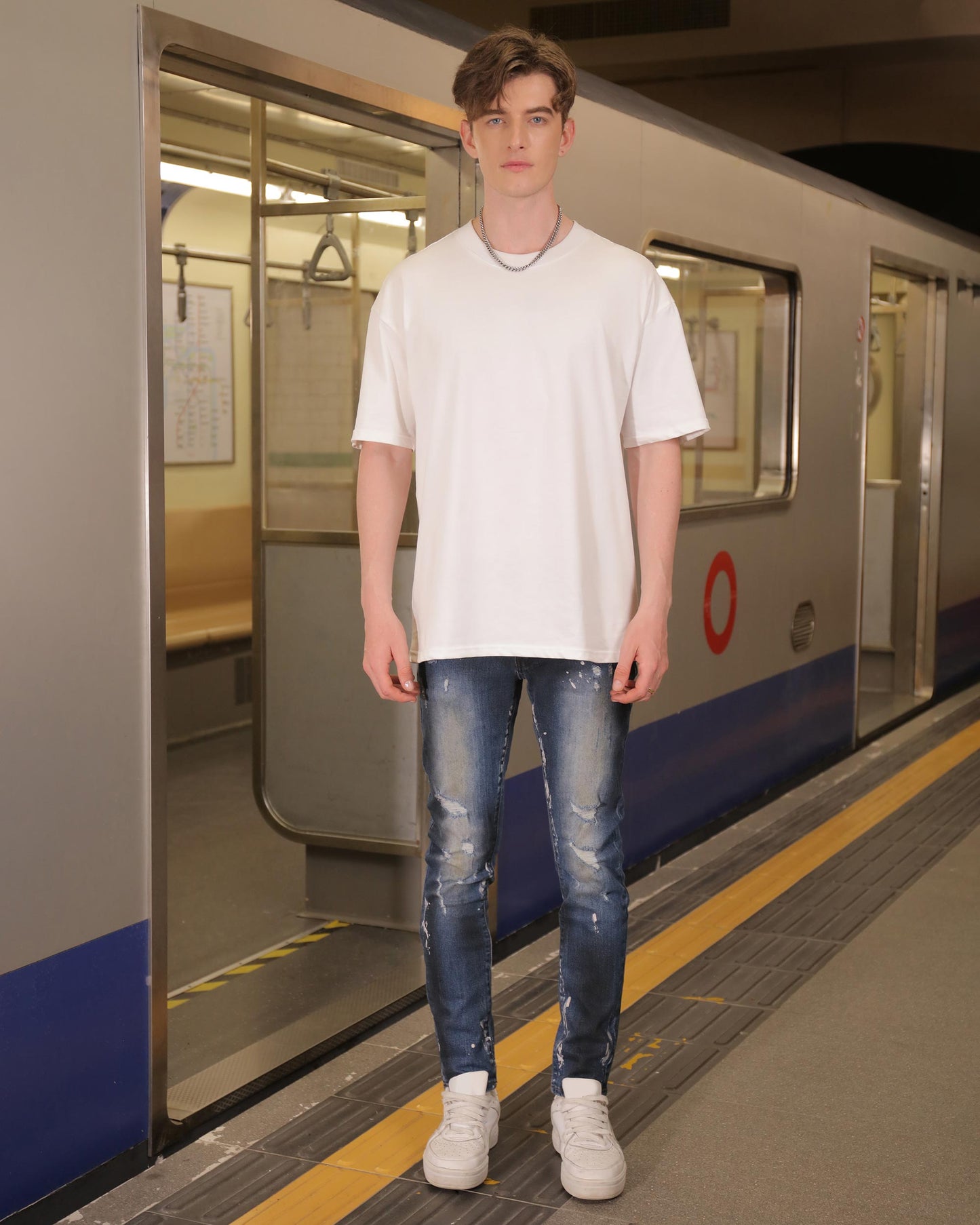 Logeqi unique blue wash jeans worn by a male model with white t-shirt and sneakers at a subway station