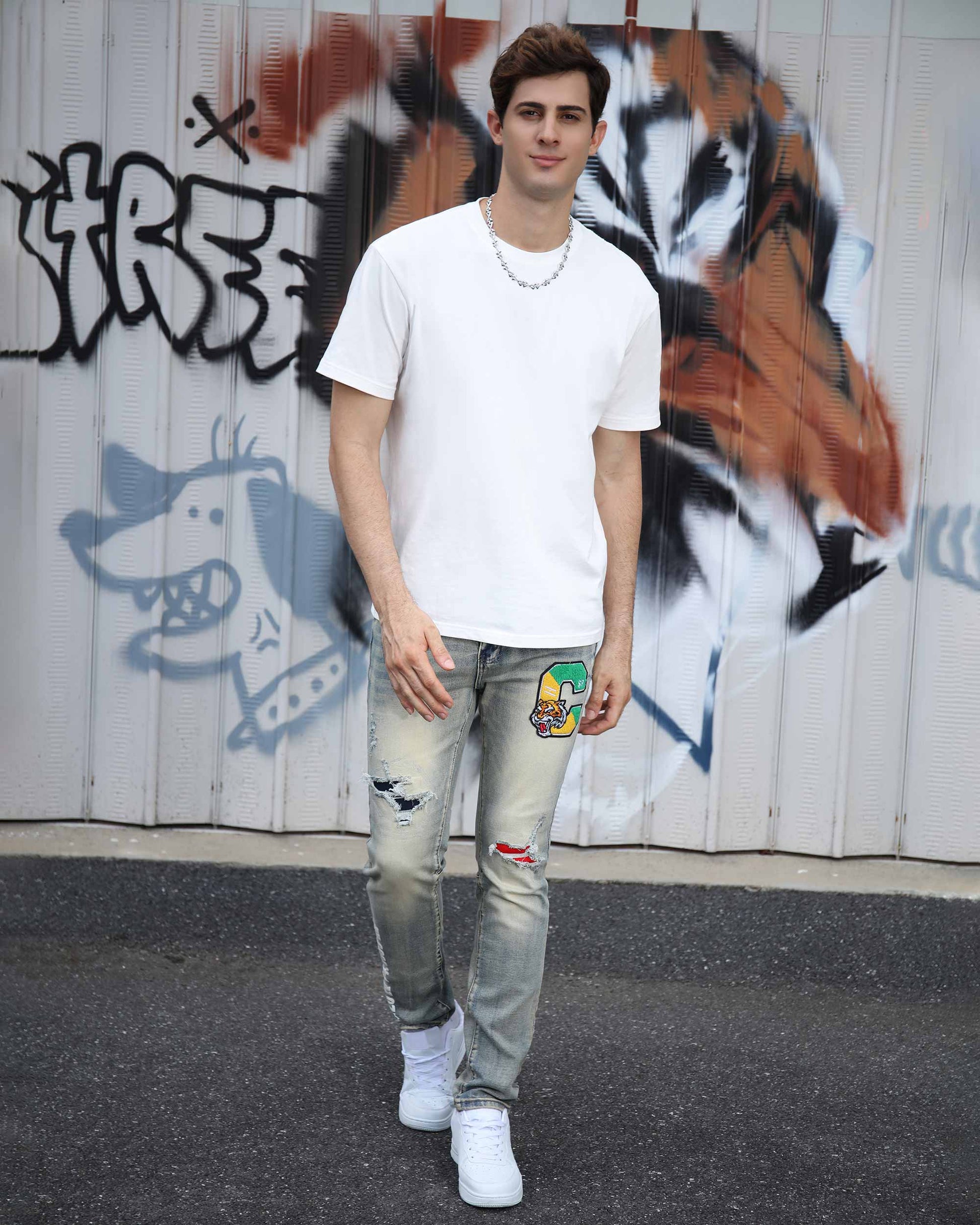 Logeqi distressed light wash jeans worn by man with patch details and ripped knees paired with white t-shirt and sneakers