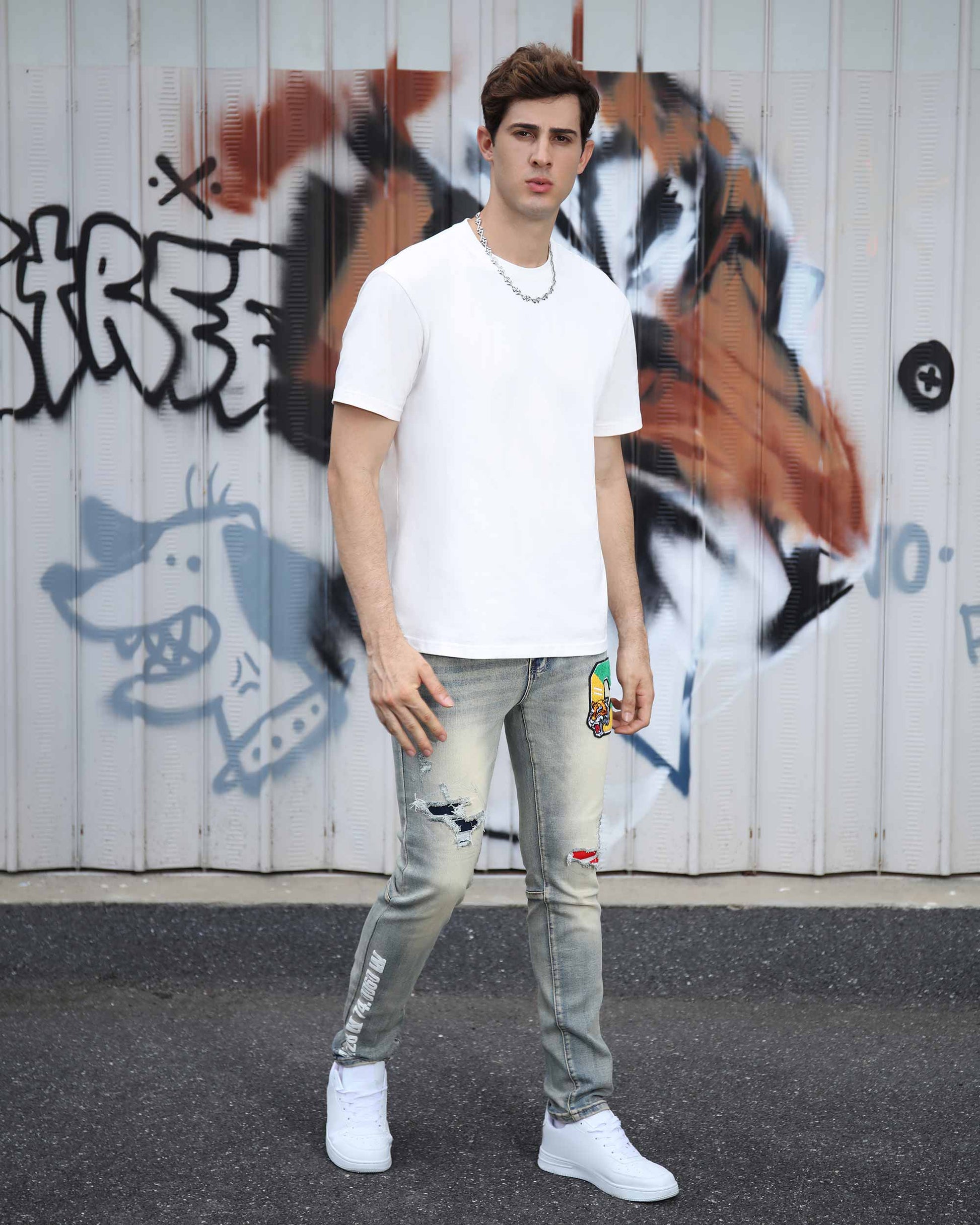 Logeqi distressed light wash jeans worn by man with graphic patches and rips paired with white sneakers