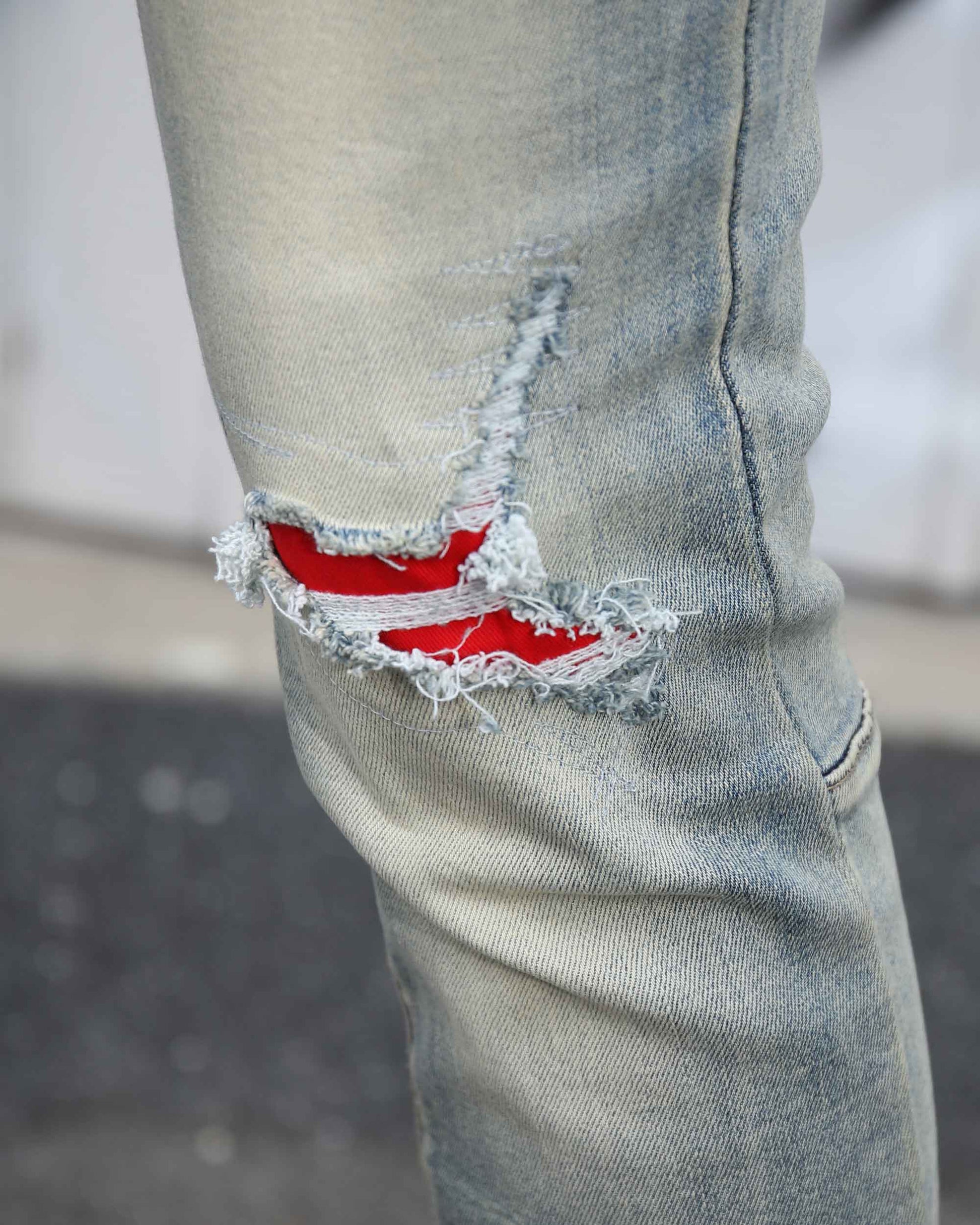 Close-up of Logeqi distressed light wash jeans with ripped detail revealing red fabric underneath