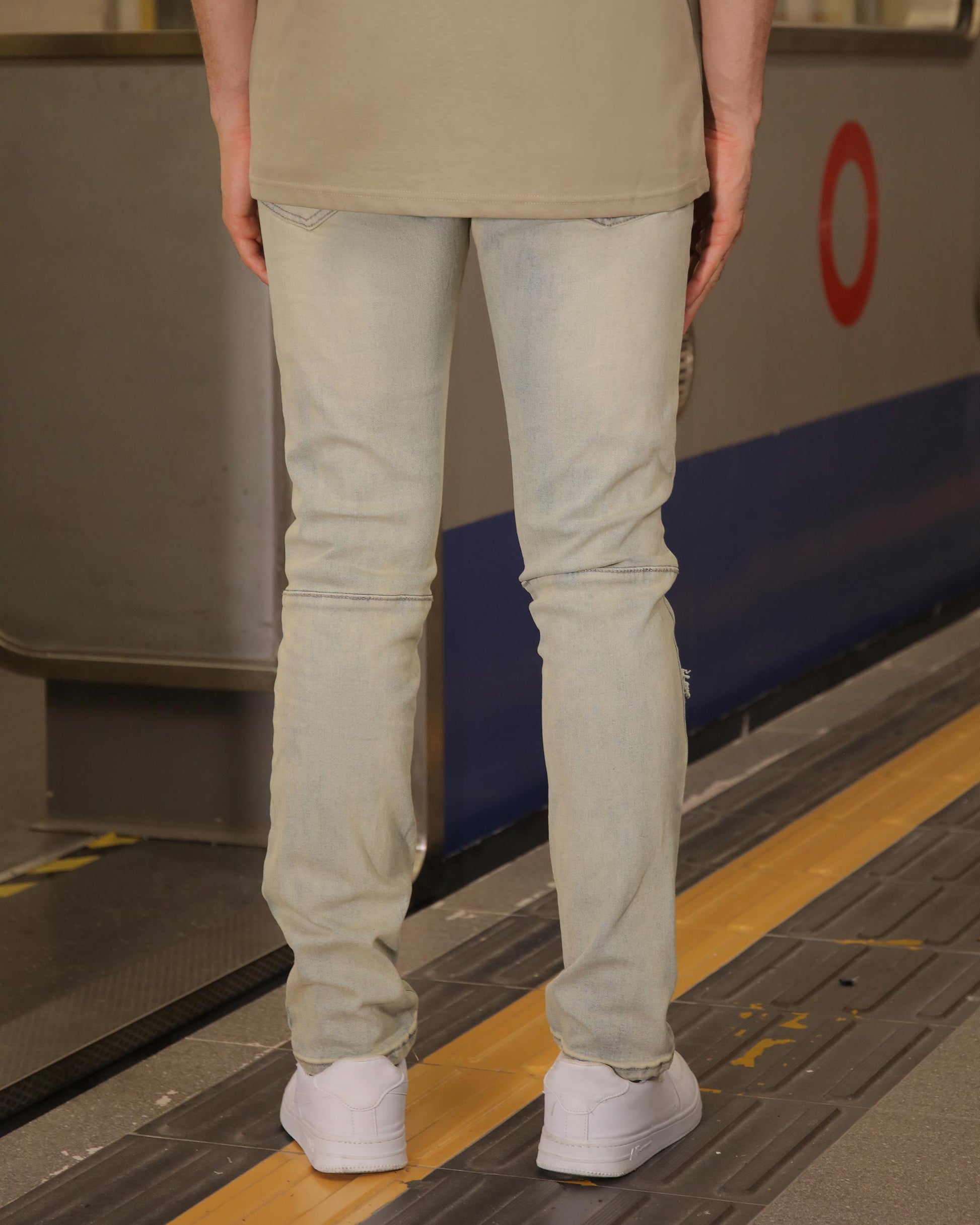 Logeqi distressed ripped blue jeans slim fit worn by model standing on subway platform