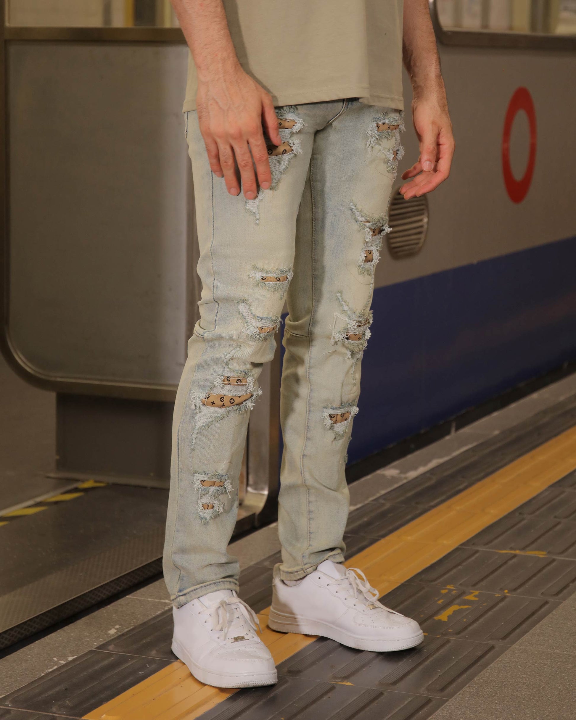 Logeqi distressed ripped blue jeans worn by a person standing on a subway platform with white sneakers