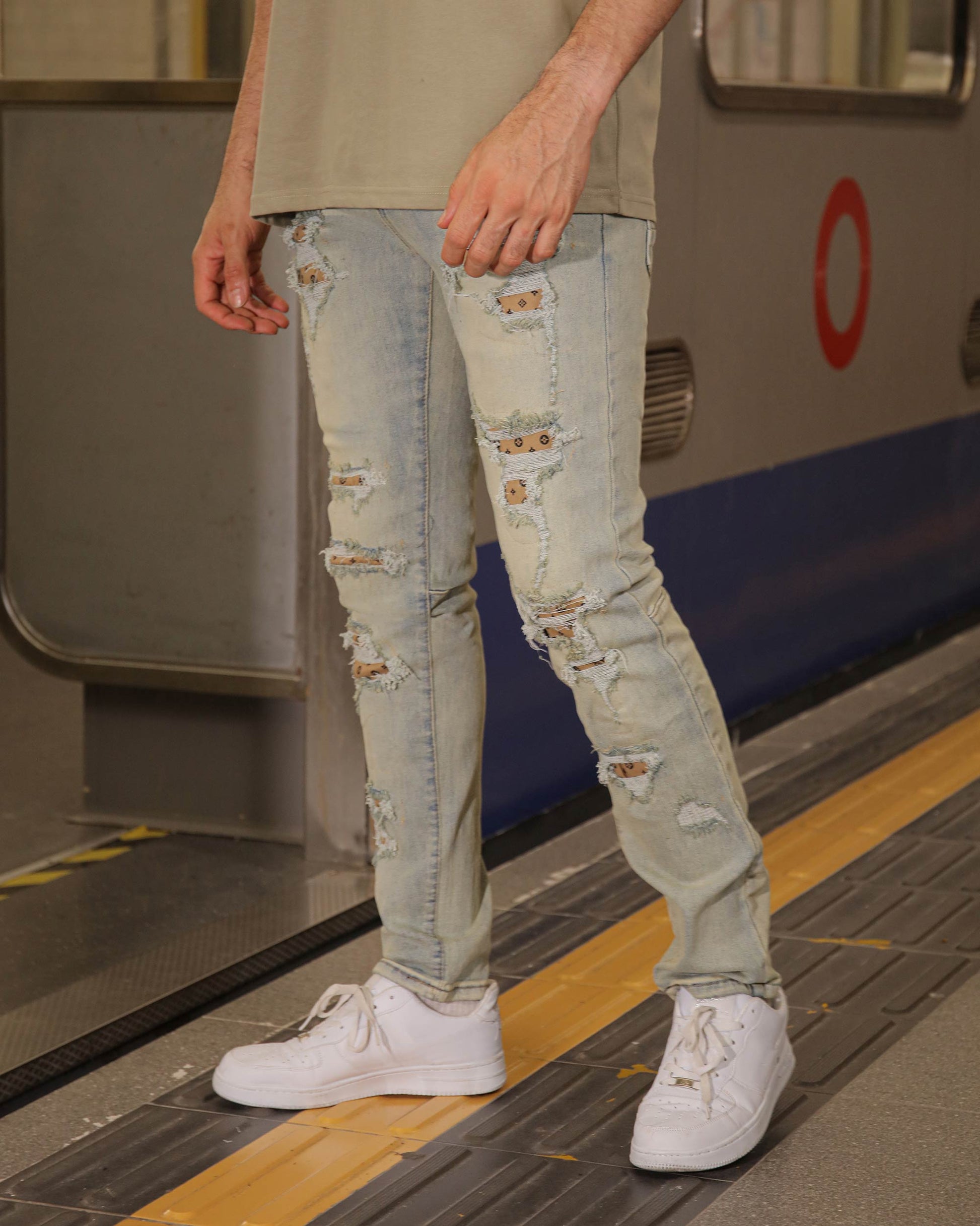 Men wearing Logeqi distressed ripped blue jeans paired with white sneakers standing on subway platform