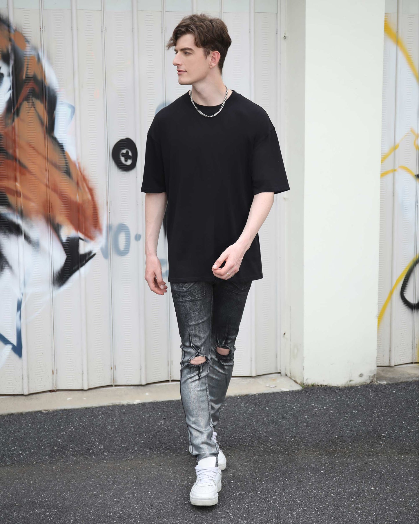 Man wearing Logeqi gradient ripped black jeans with a black t-shirt and white sneakers walking outdoors