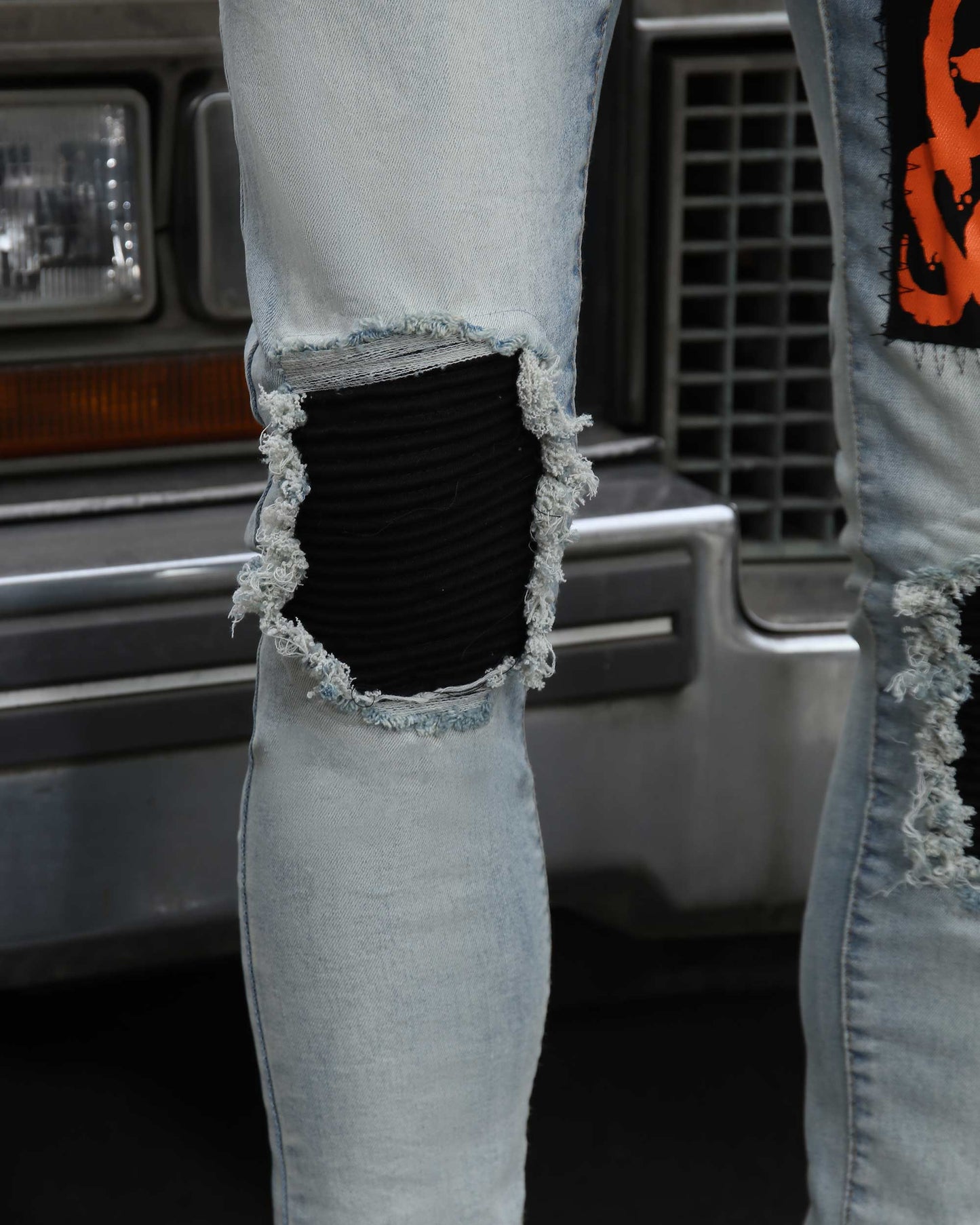 Close-up of Logeqi light wash graffiti jeans with ripped knee and black patch detailing