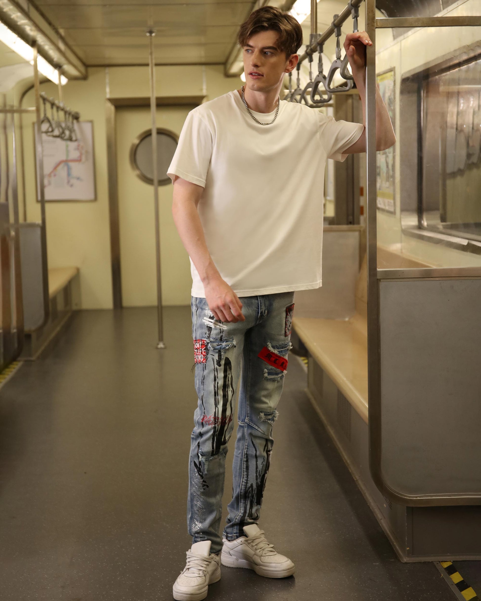 Man wearing Logeqi medium wash ripped jeans with patches and white sneakers in subway train