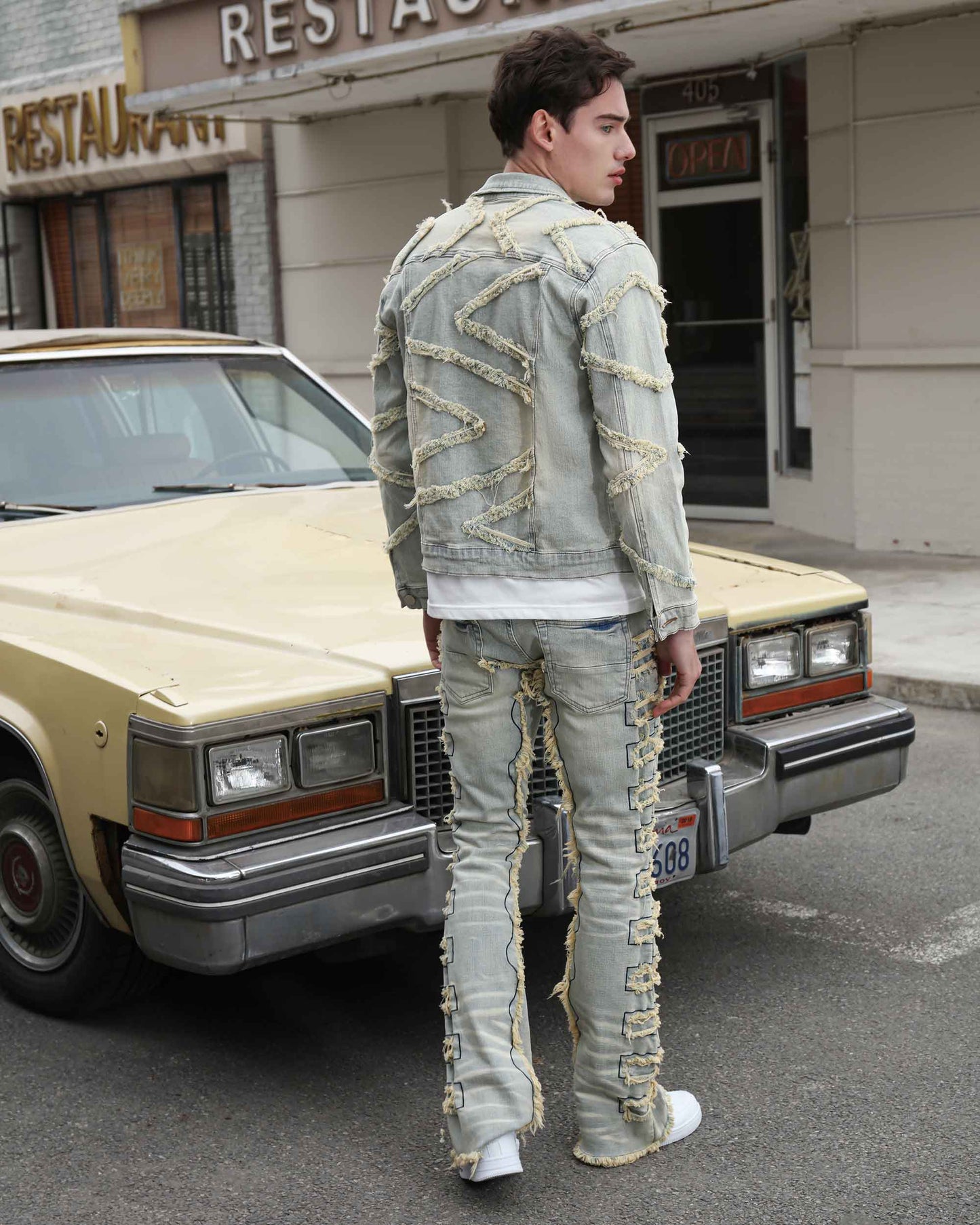 Logeqi vintage blue stacked jeans with frayed detailing worn by a man standing next to a vintage car