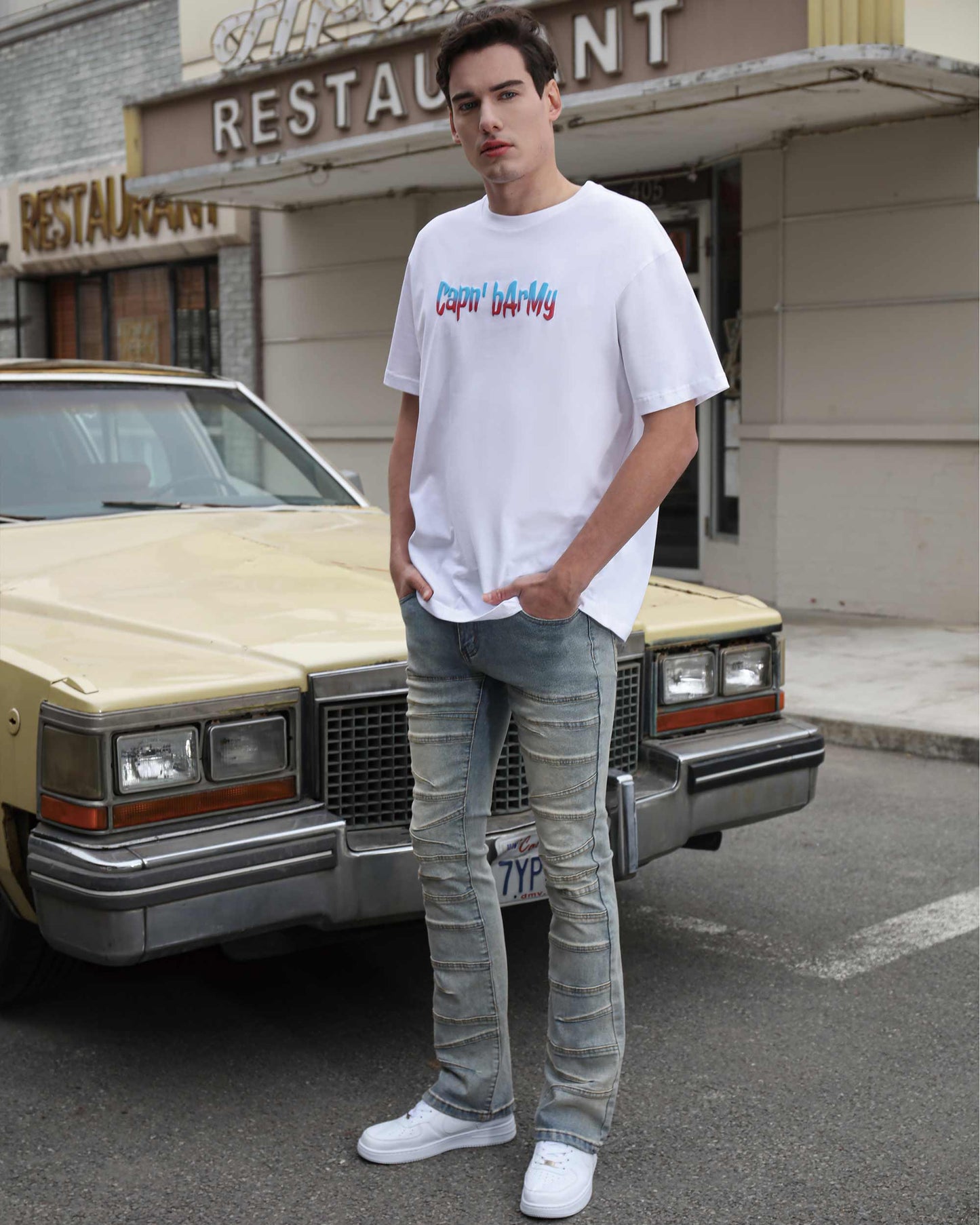 Man wearing vintage distressed blue jeans by Logeqi paired with white graphic t-shirt and sneakers outdoors