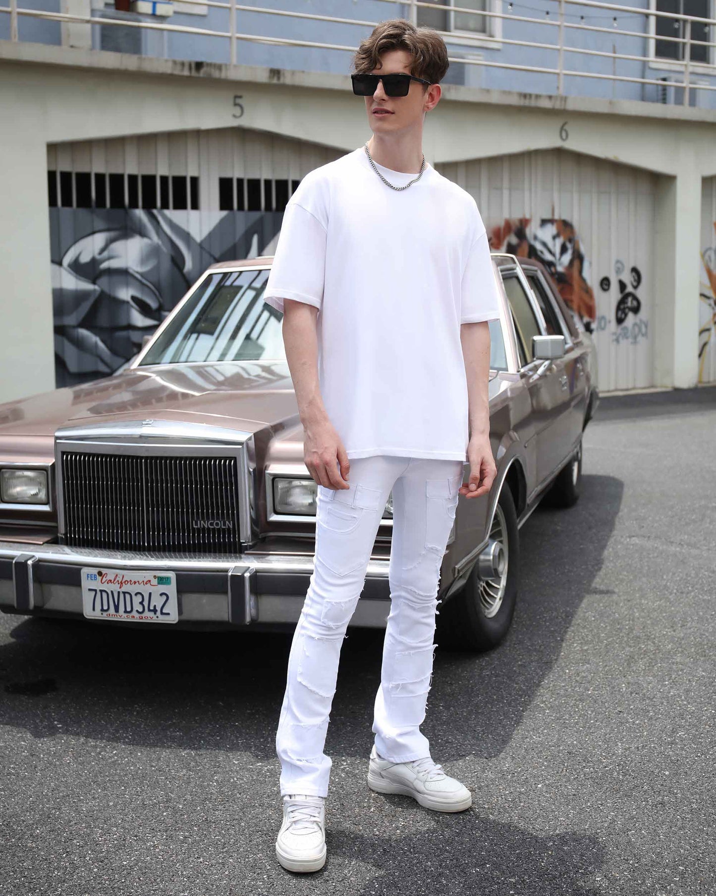 Man wearing vintage white flared jeans styled with an oversized white t-shirt against a classic car