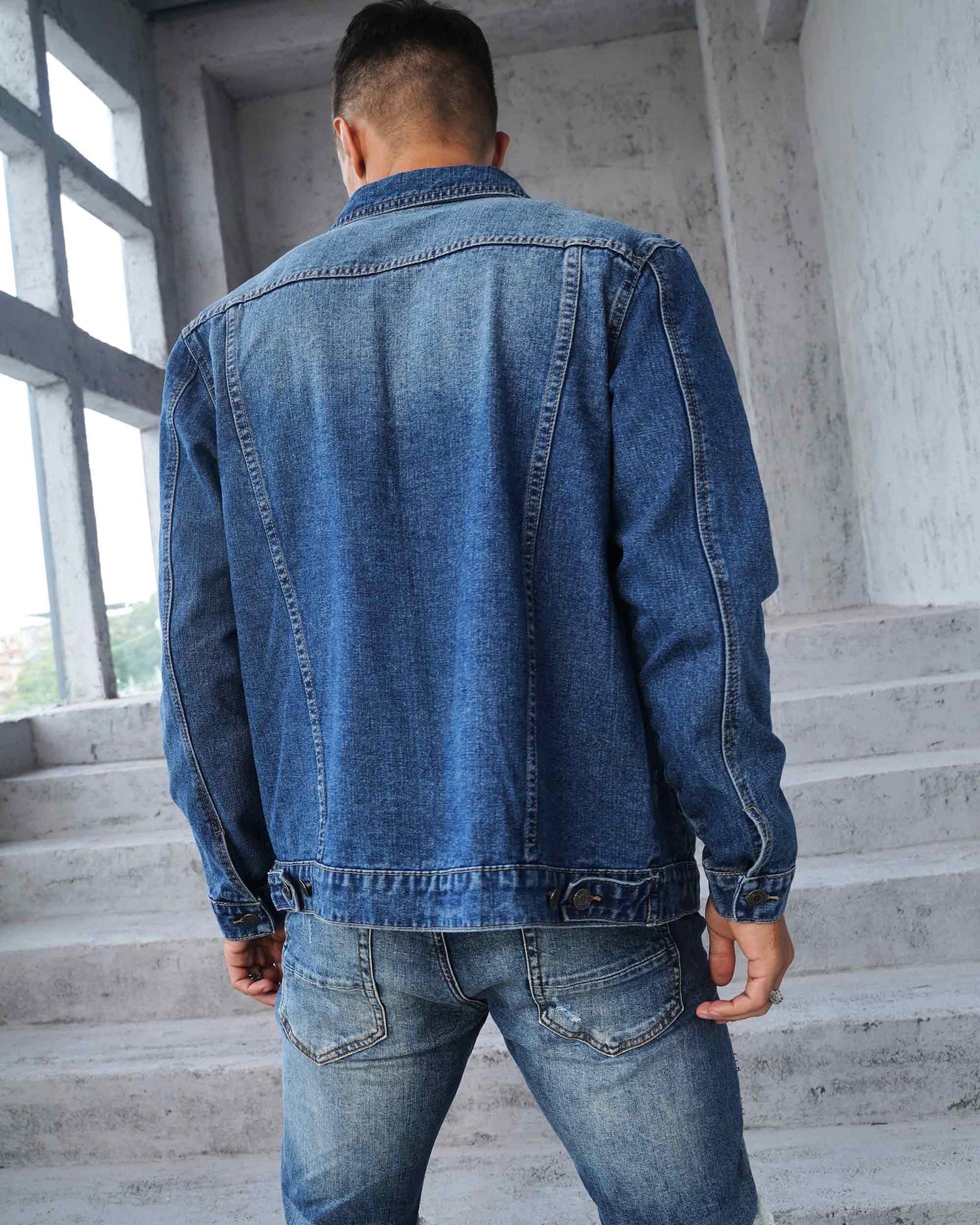 Back view of a Logeqi washed blue denim jacket on a model standing on stairs