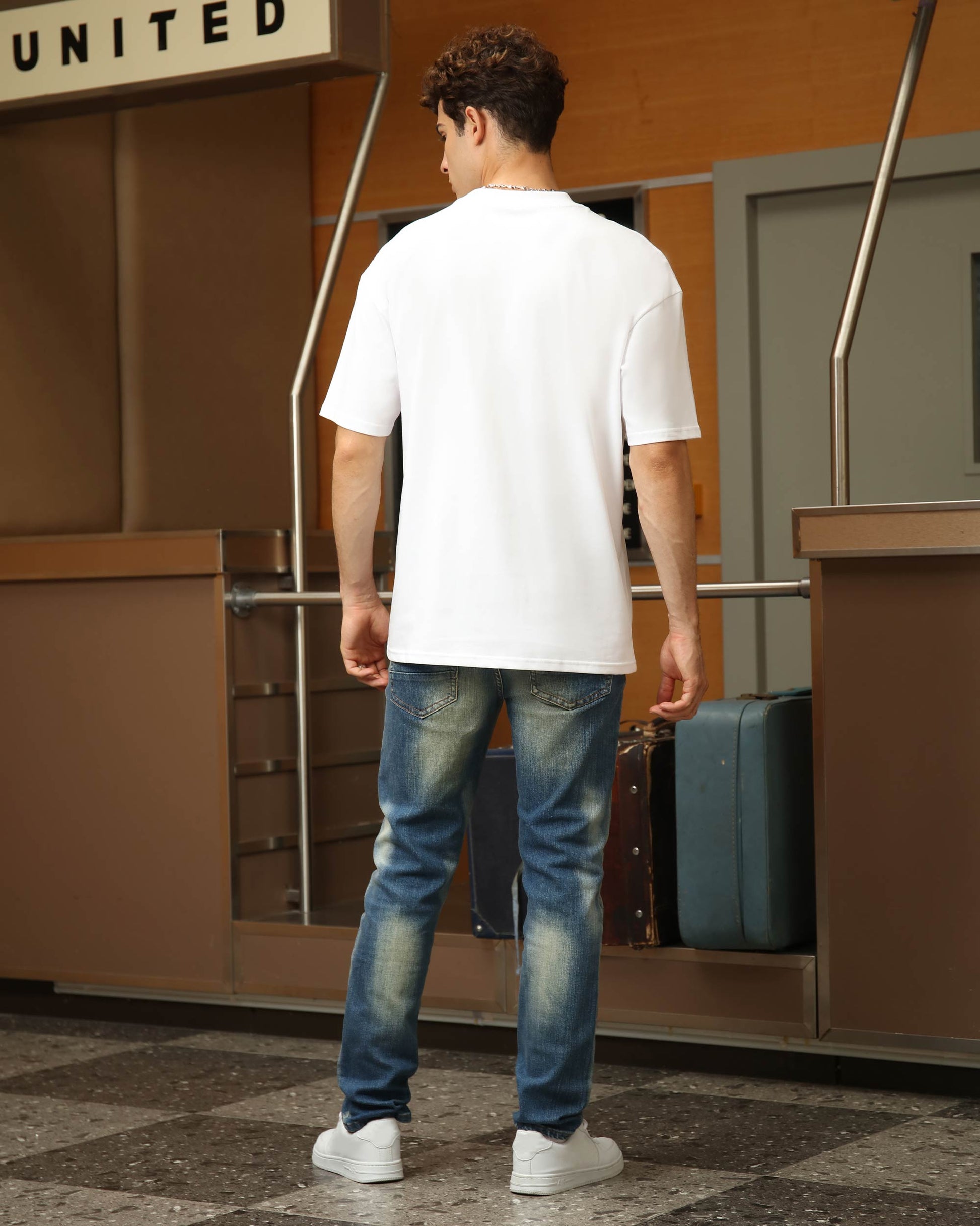 Back view of a man wearing Logeqi whiskered distressed jeans styled with a white t-shirt