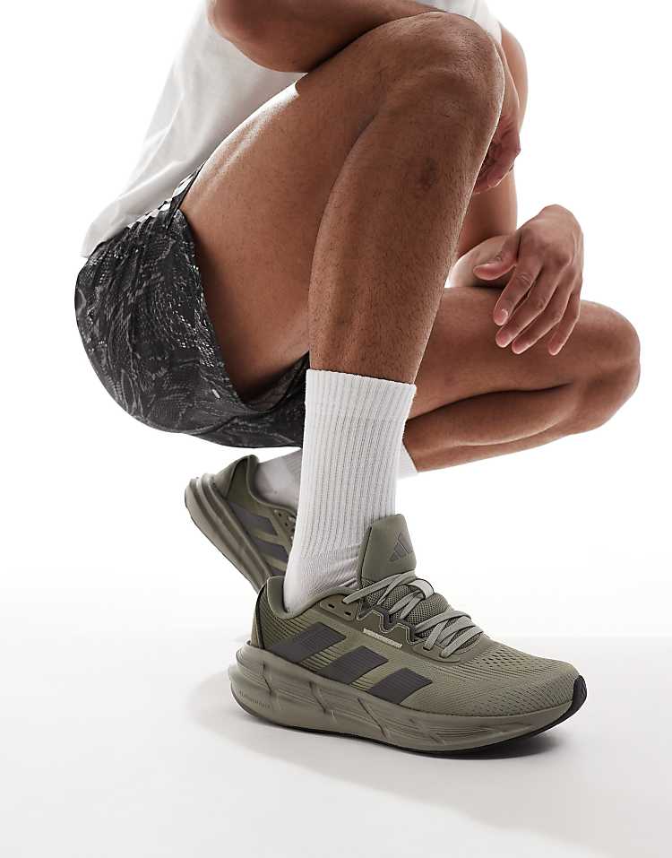 adidas Questar 3 olive green sneakers showcased on a model kneeling in sporty attire