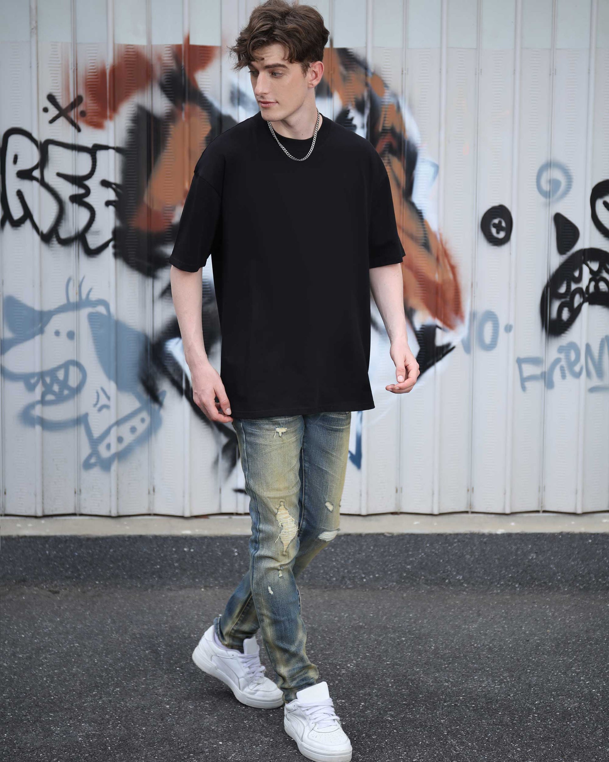 Man wearing a black cotton t-shirt with a relaxed fit, paired with distressed jeans for a casual look