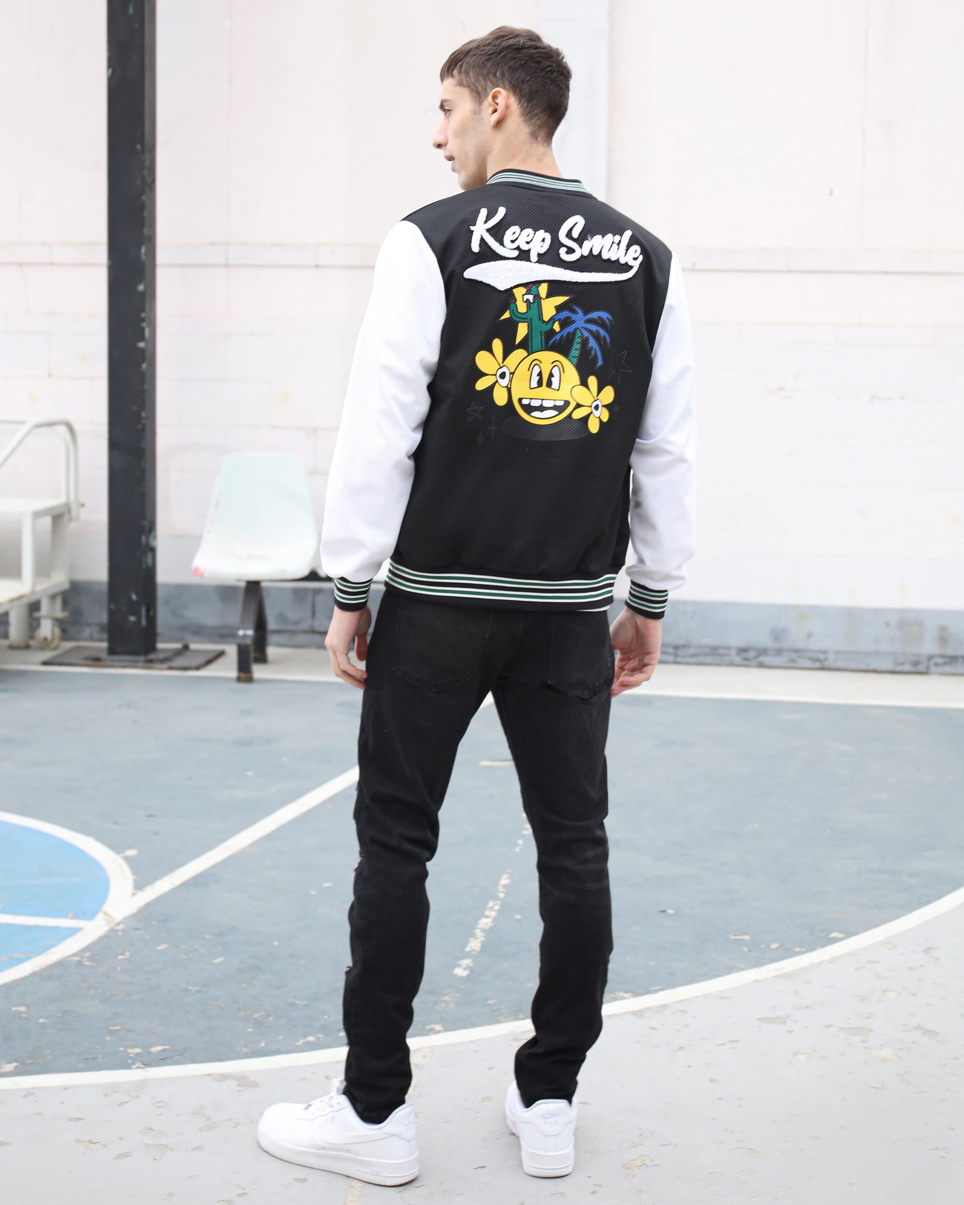 Man wearing black graffiti slim-fit jeans with a stylish varsity jacket for a trendy streetwear look