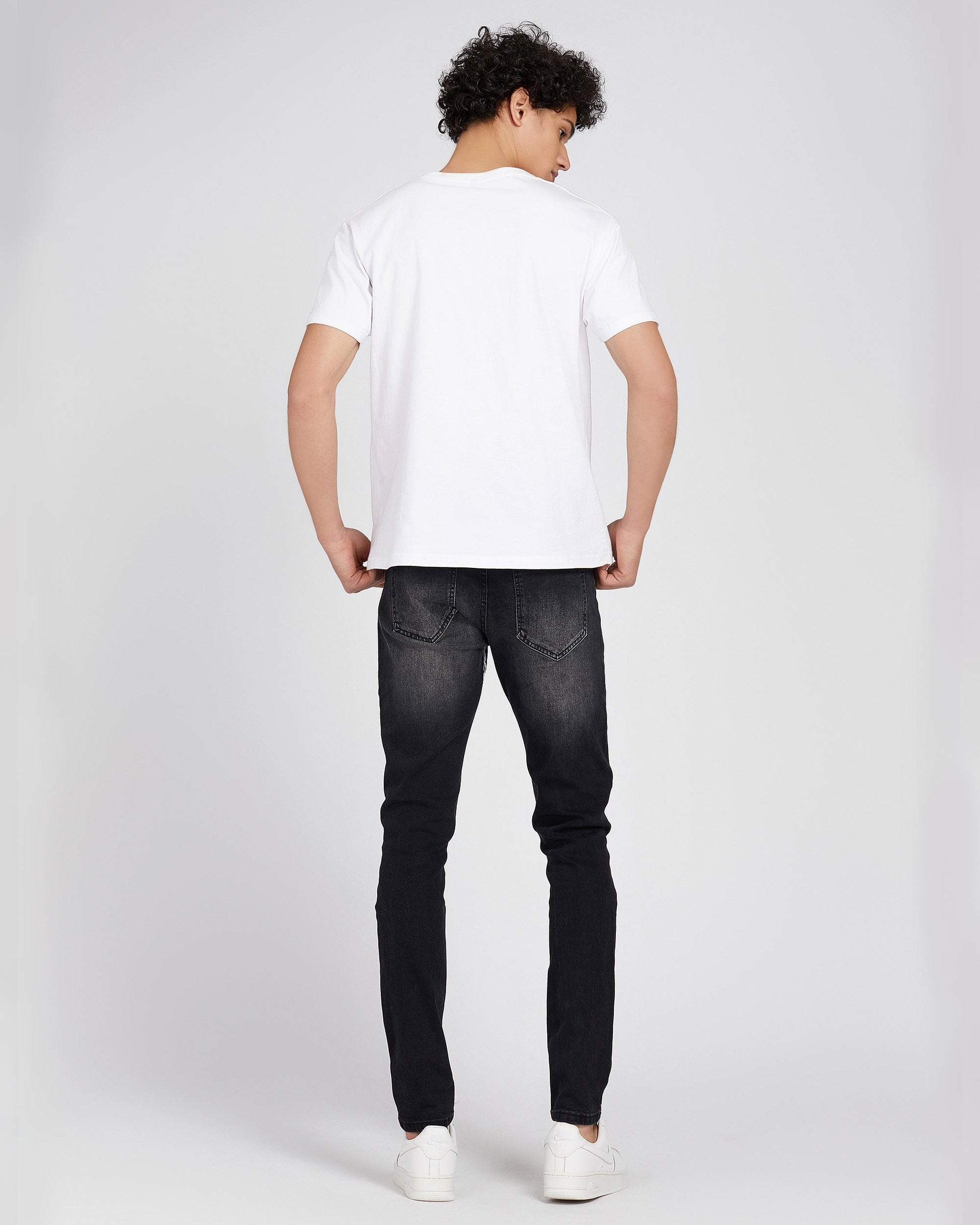Man wearing Logeqi black ripped graffiti jeans with white t-shirt and sneakers viewed from back