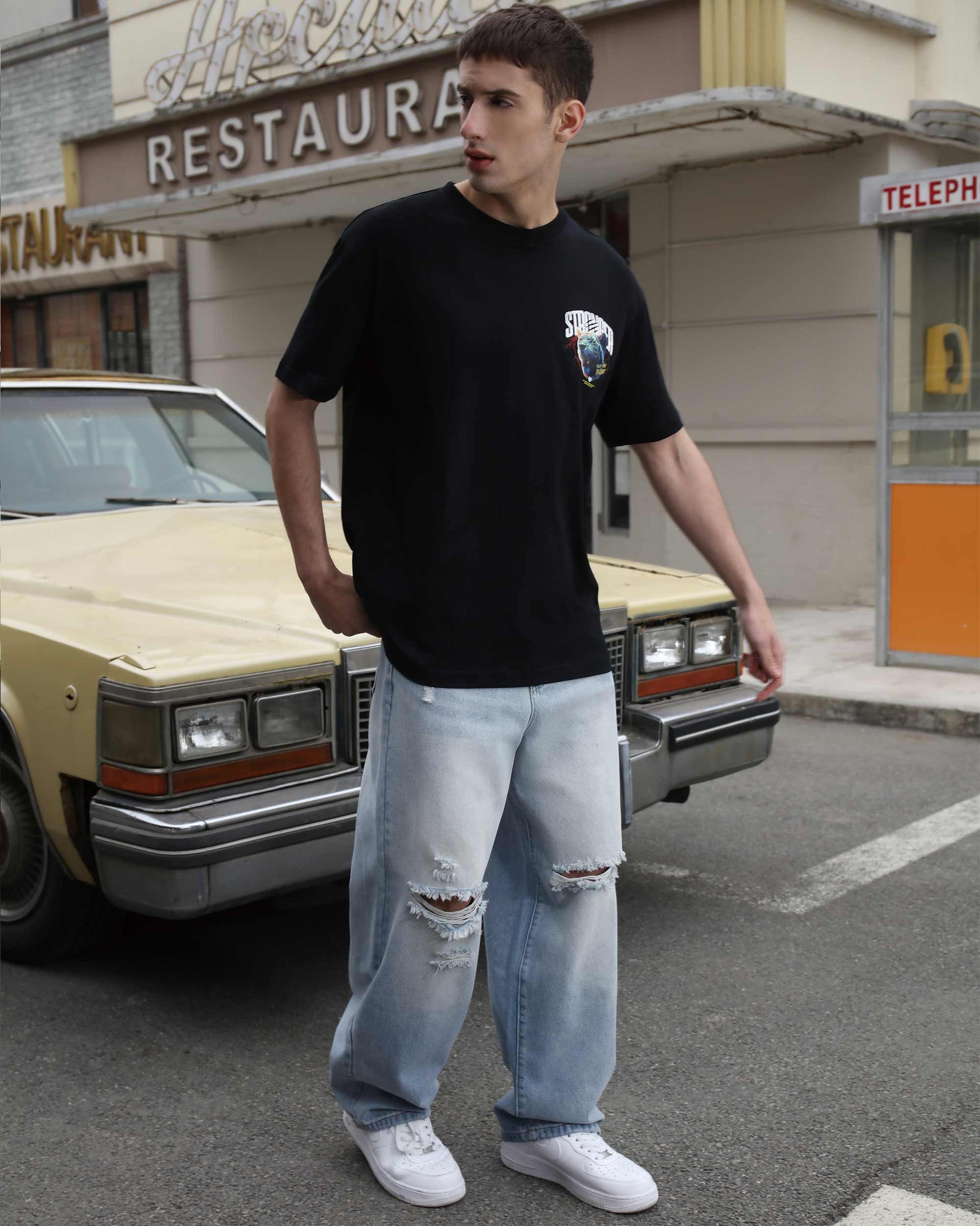 Logeqi blue ripped baggy jeans worn by man standing next to vintage car on street