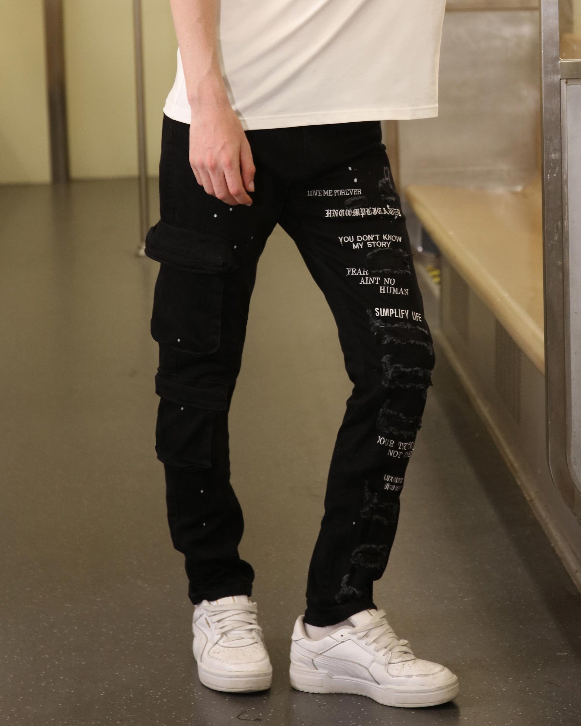 Logeqi black spray paint detail jeans with white text print and cargo pockets worn with white sneakers