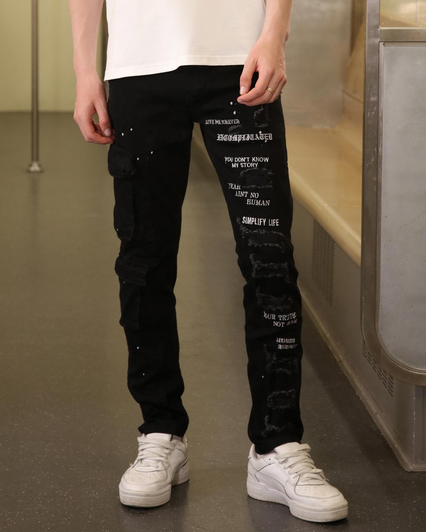 Logeqi black spray paint detail jeans with white text and distressed patches worn with white sneakers