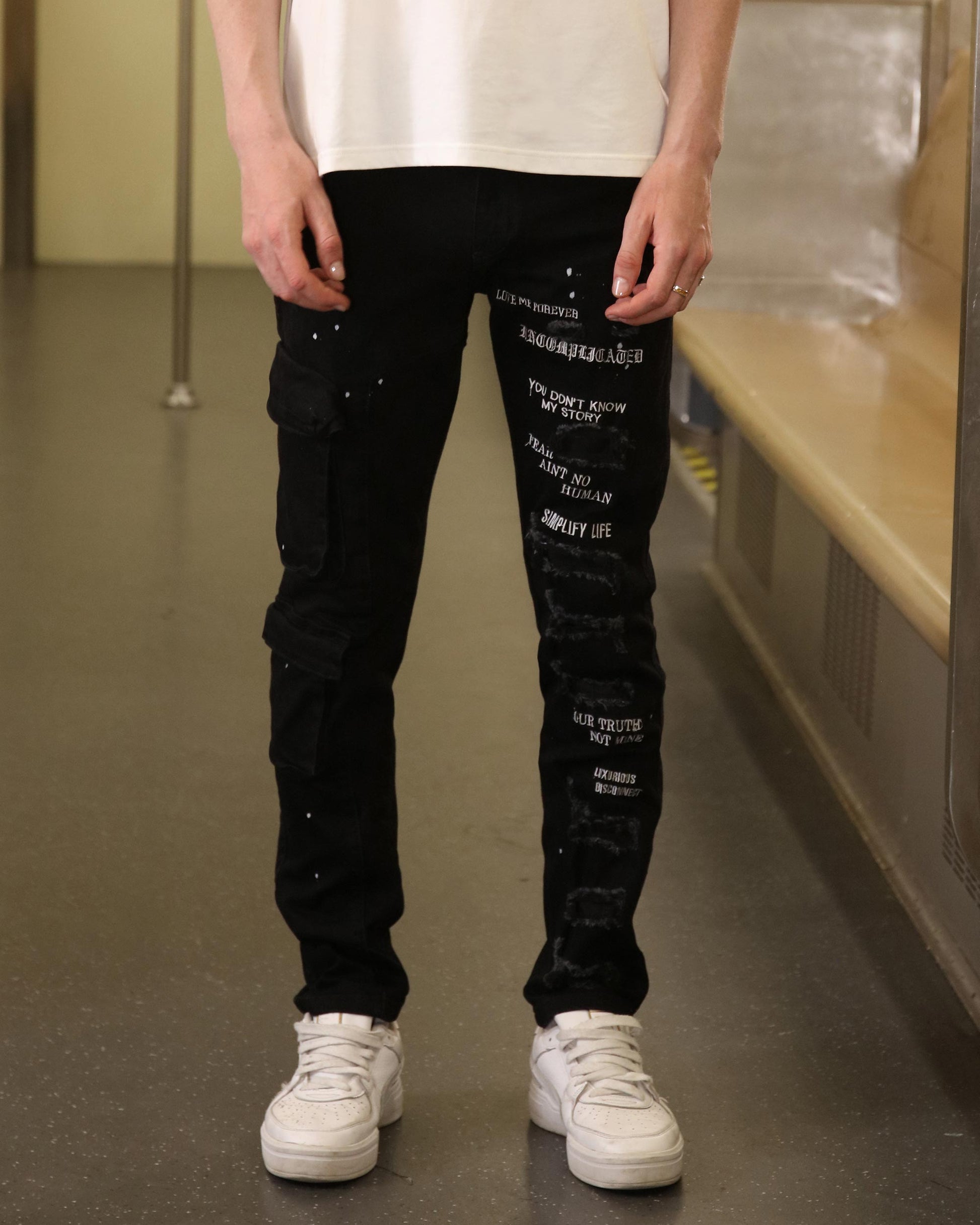 Logeqi black spray paint detail jeans with white graphic text and cargo pockets worn with white sneakers