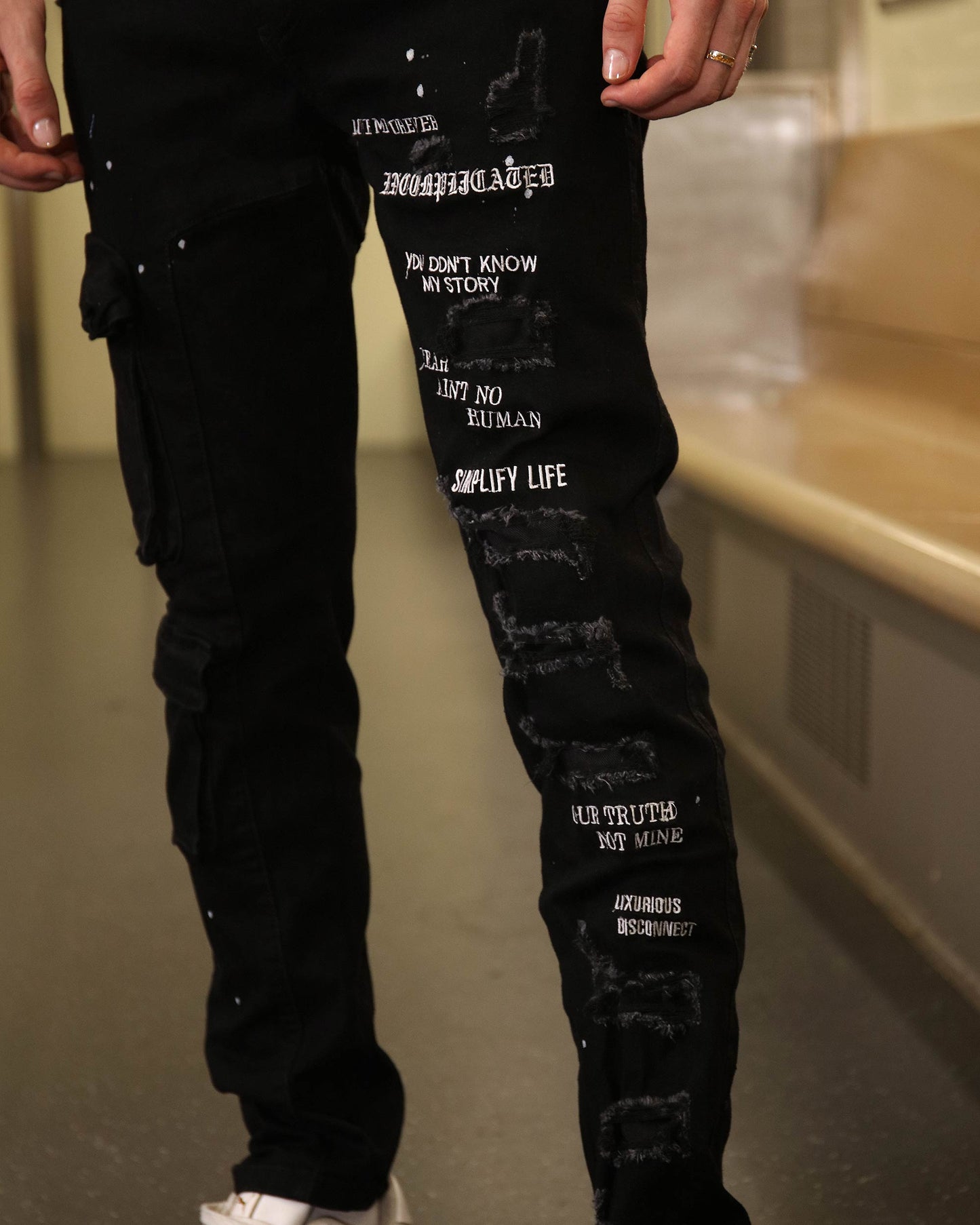 Logeqi spray paint detail jeans in black with white text prints and distressed patches on legs