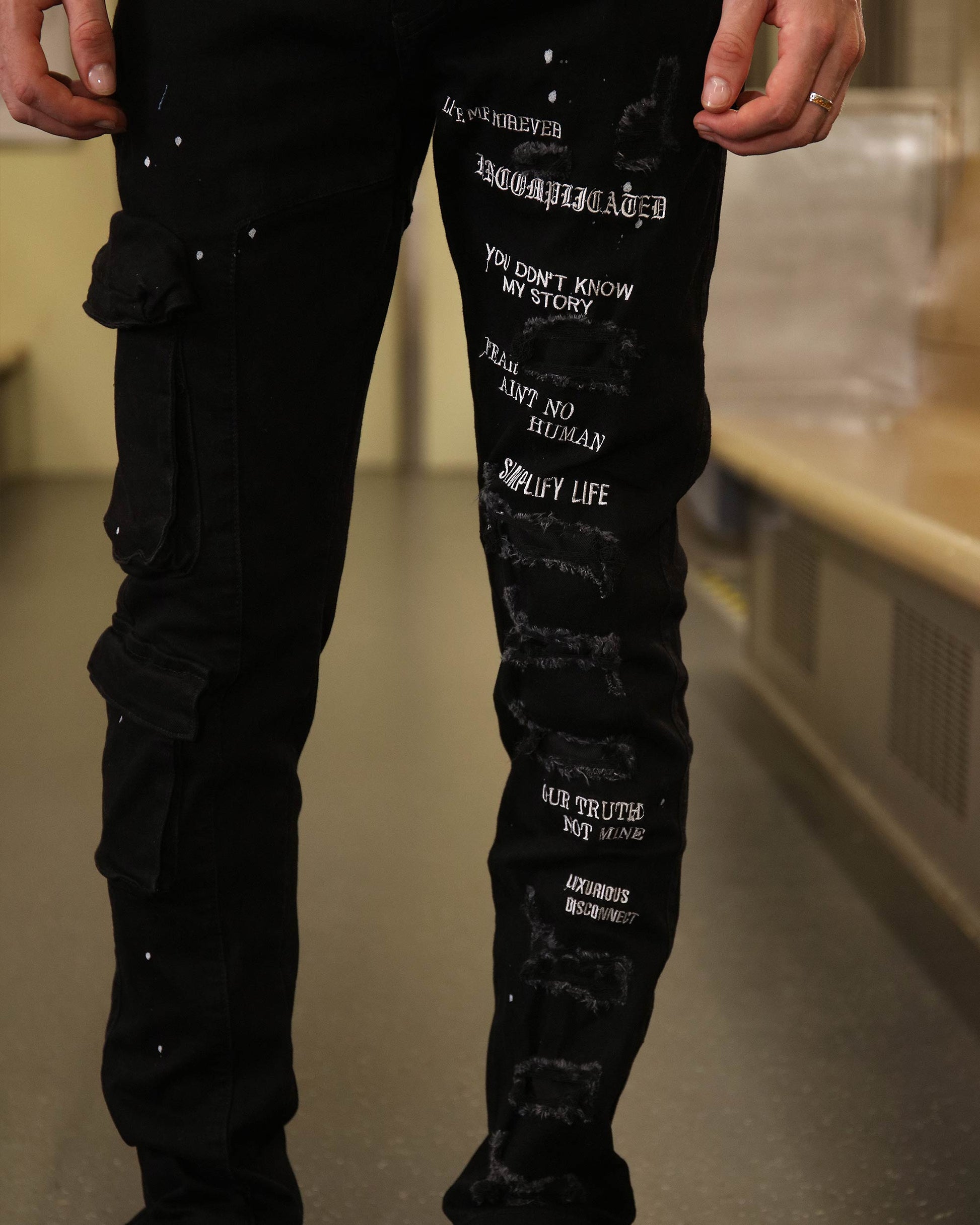 Logeqi black spray paint detail jeans with white text and distressed patches on the legs