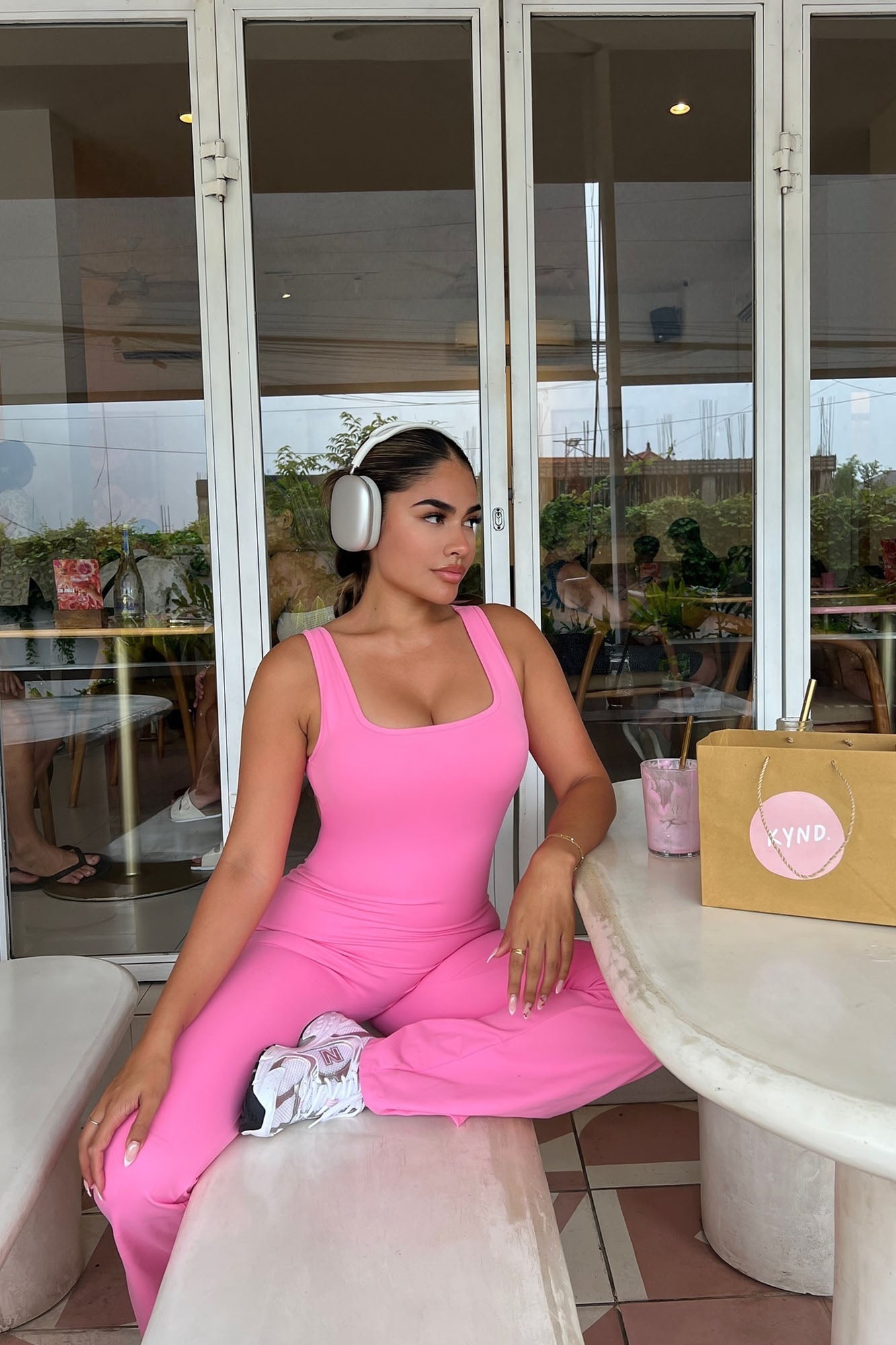 Model wearing a bubblegum pink active jumpsuit styled with headphones at a cafe