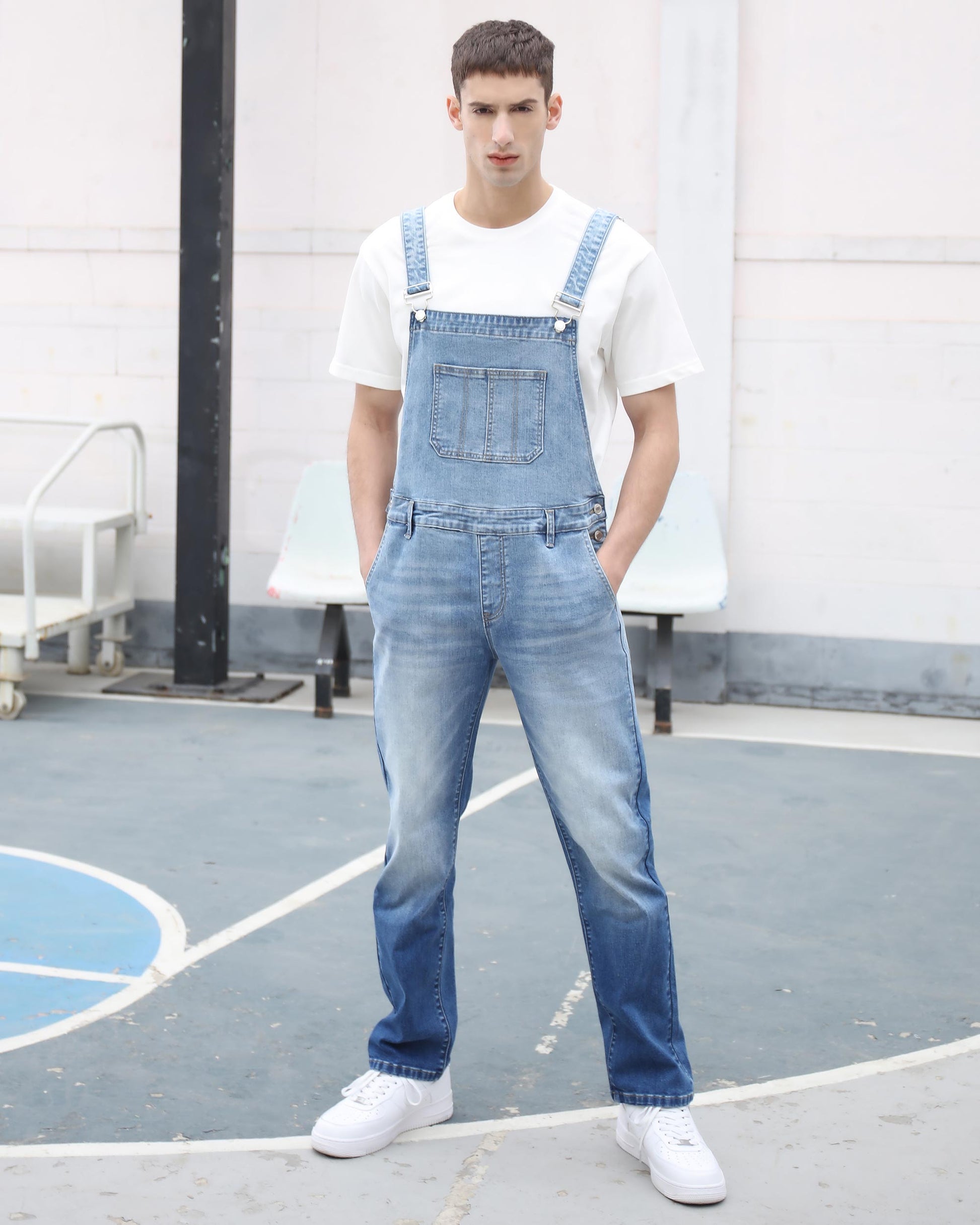 Man wearing Logeqi classic denim overalls in light blue paired with white sneakers and a white t-shirt