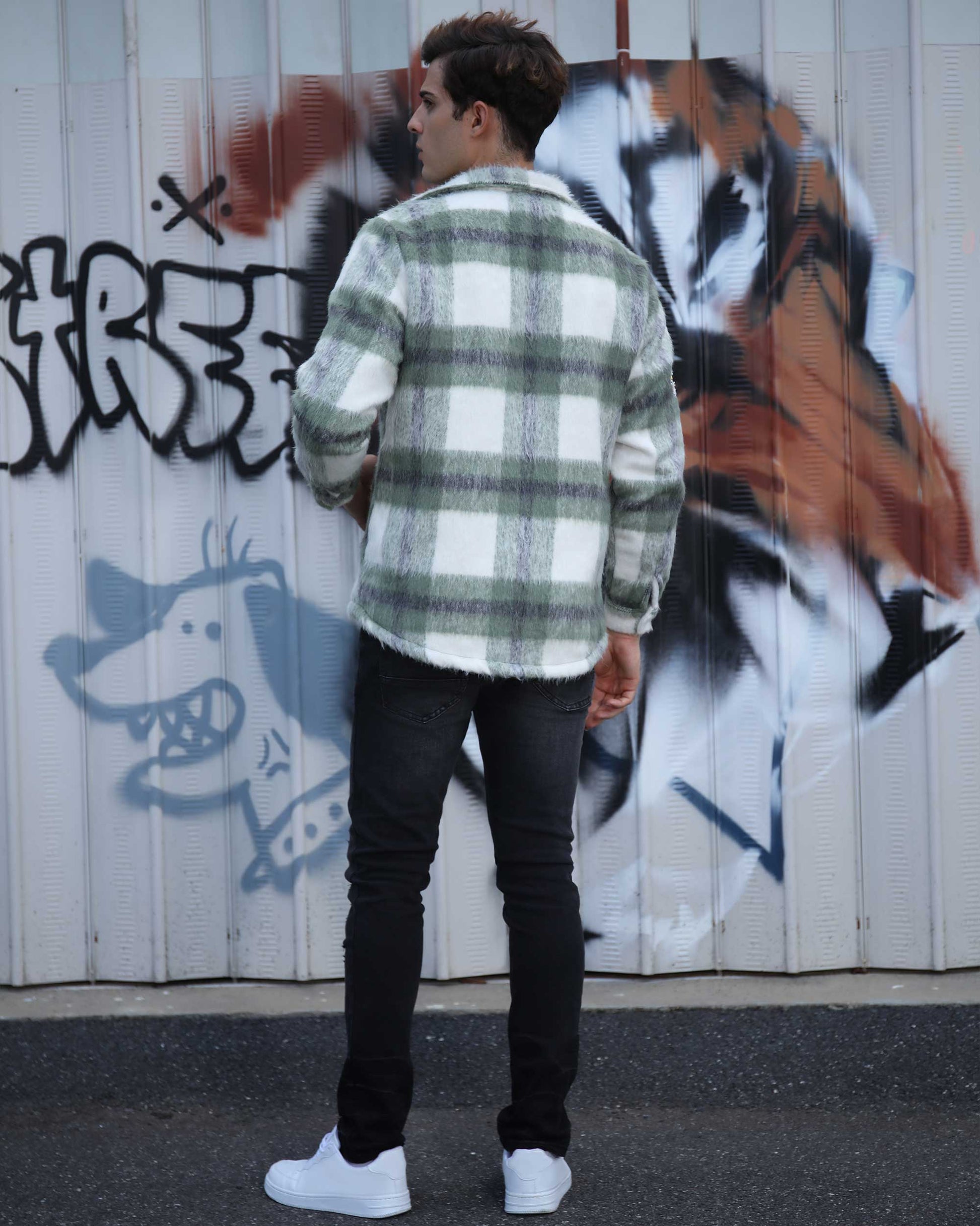 Man wearing Logeqi classic plaid moto jacket in green and white standing against graffiti wall