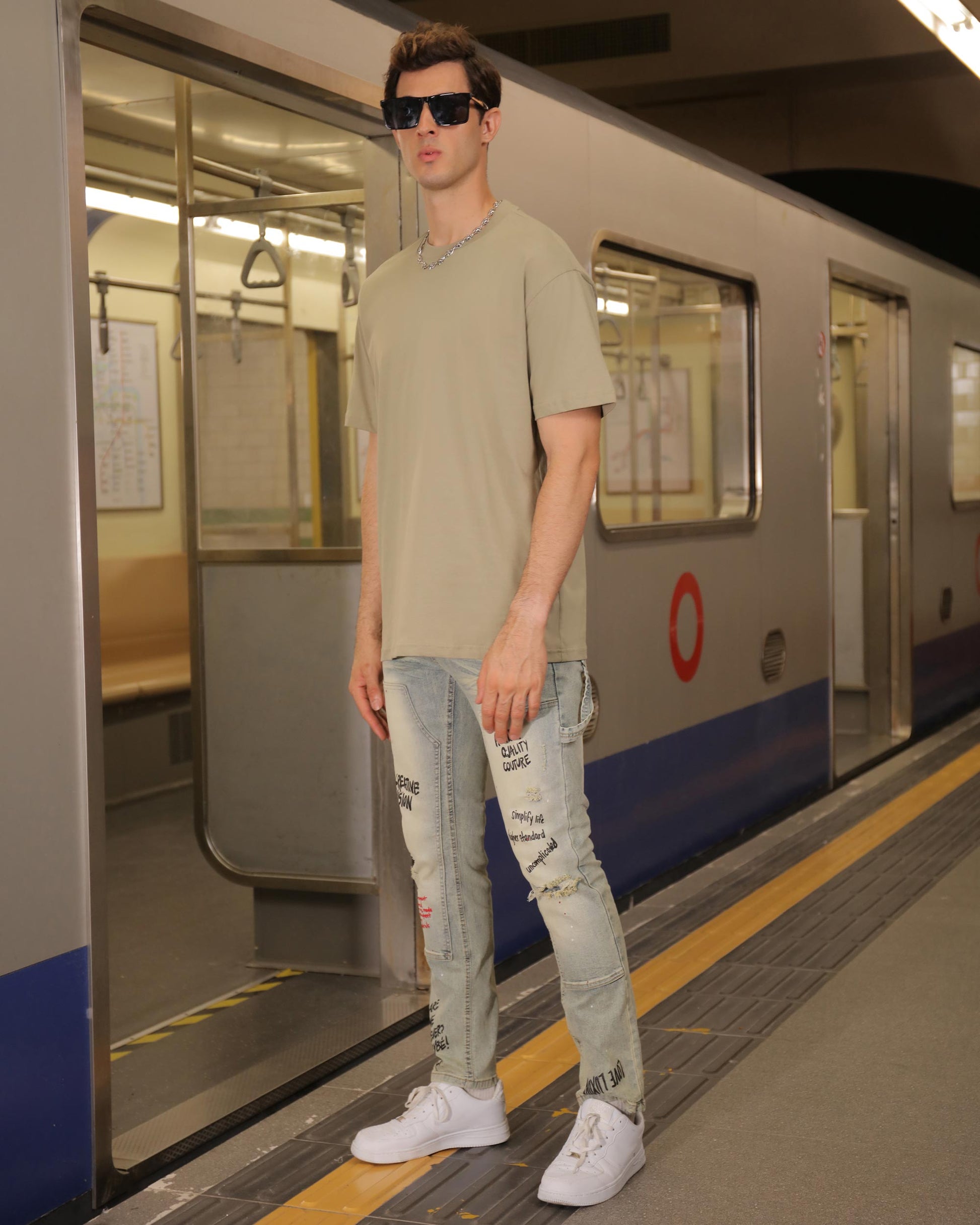 Logeqi essential solid tee in olive green worn by a model in a subway station with distressed jeans