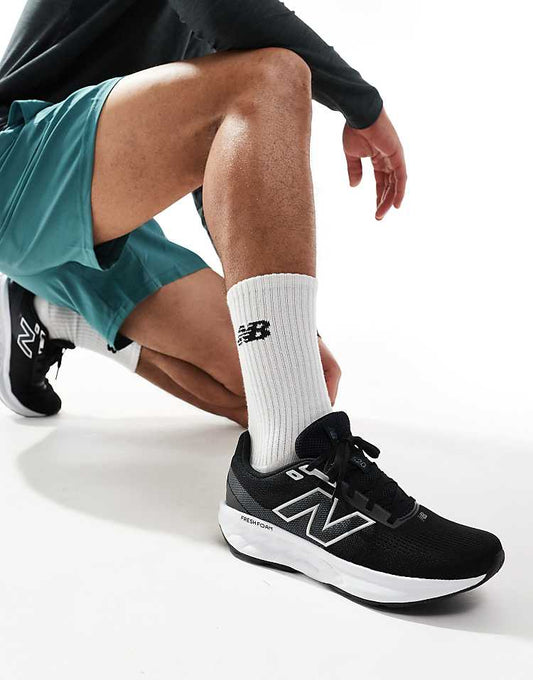 New Balance 520 running shoes in black worn by a man kneeling in blue shorts and white New Balance socks