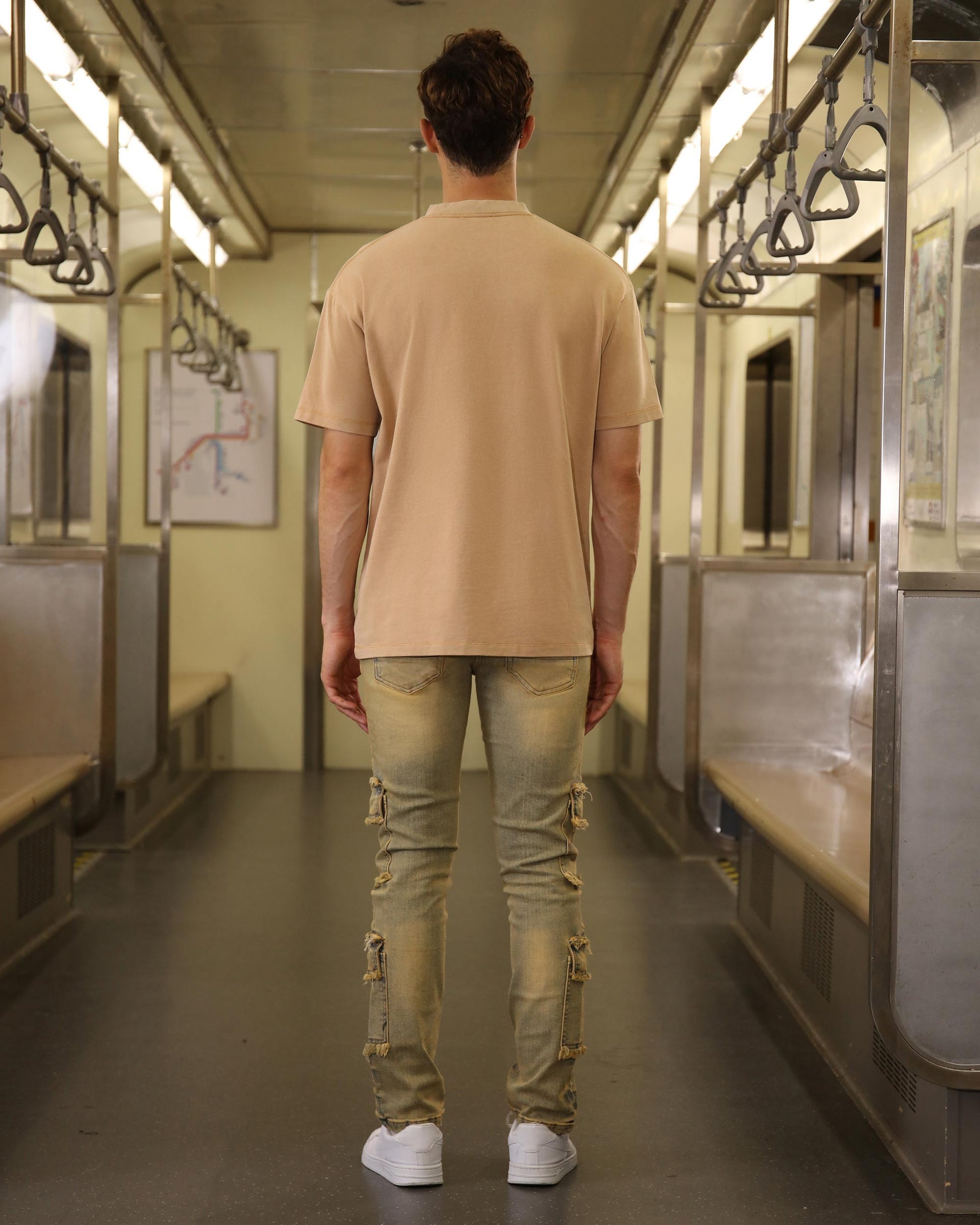 Back view of a man wearing Logeqi raw edge brown jeans with cargo pockets inside a subway train