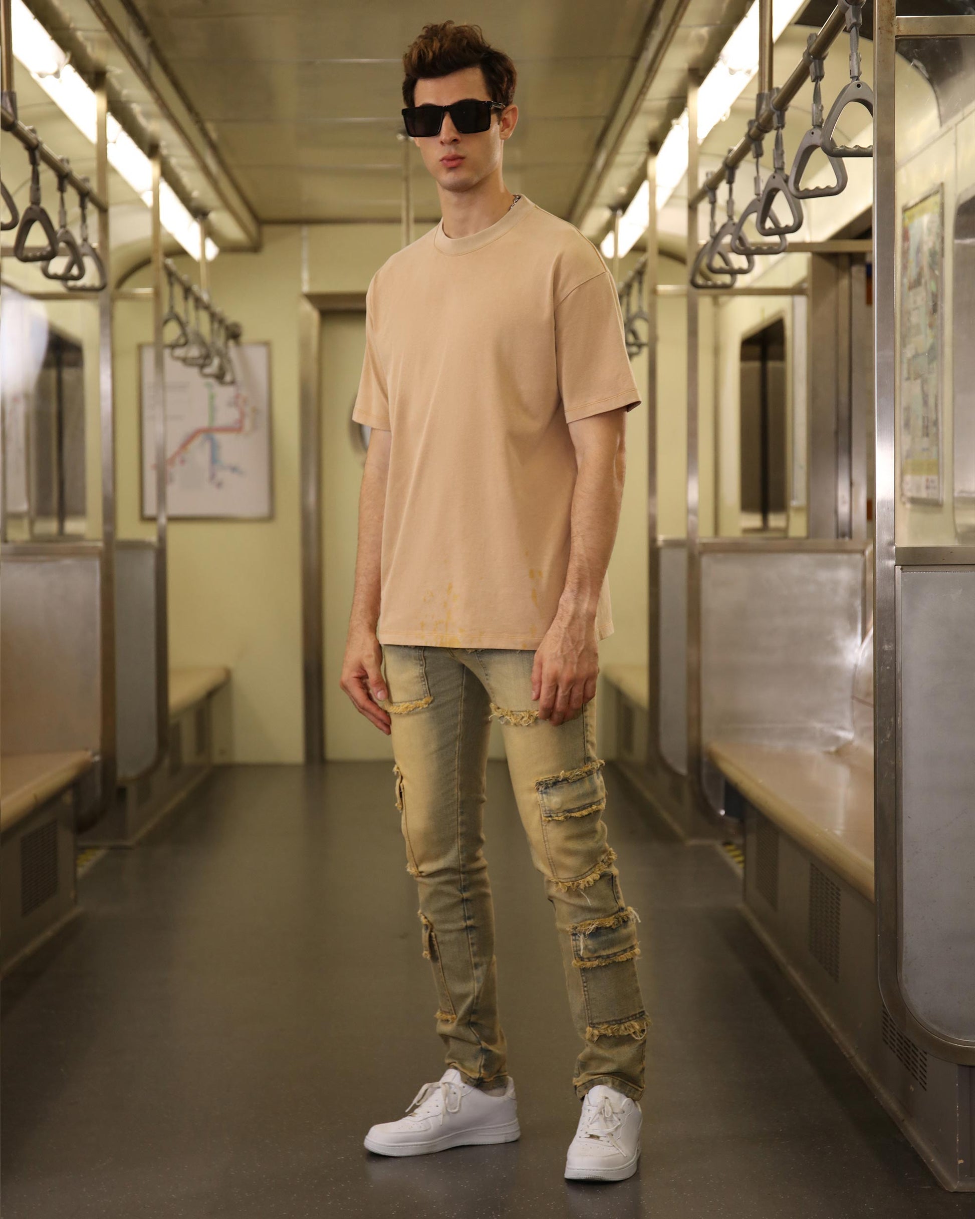 Logeqi raw edge brown jeans with distressed details worn by a male model in a subway train