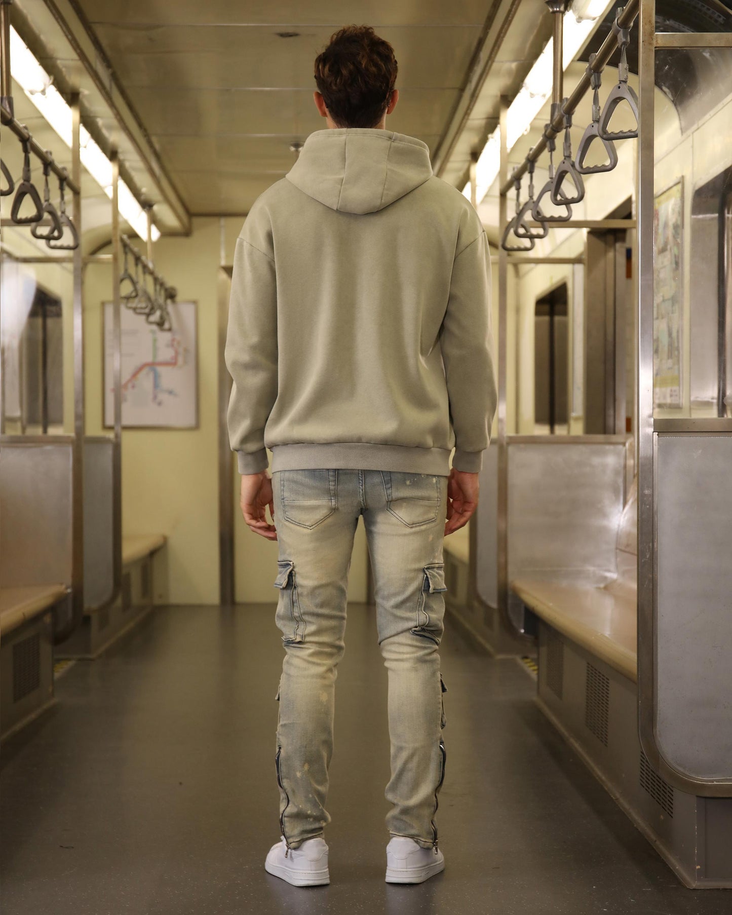 Logeqi spray painted blue cargo jeans worn by man standing in subway train with gray hoodie and white sneakers