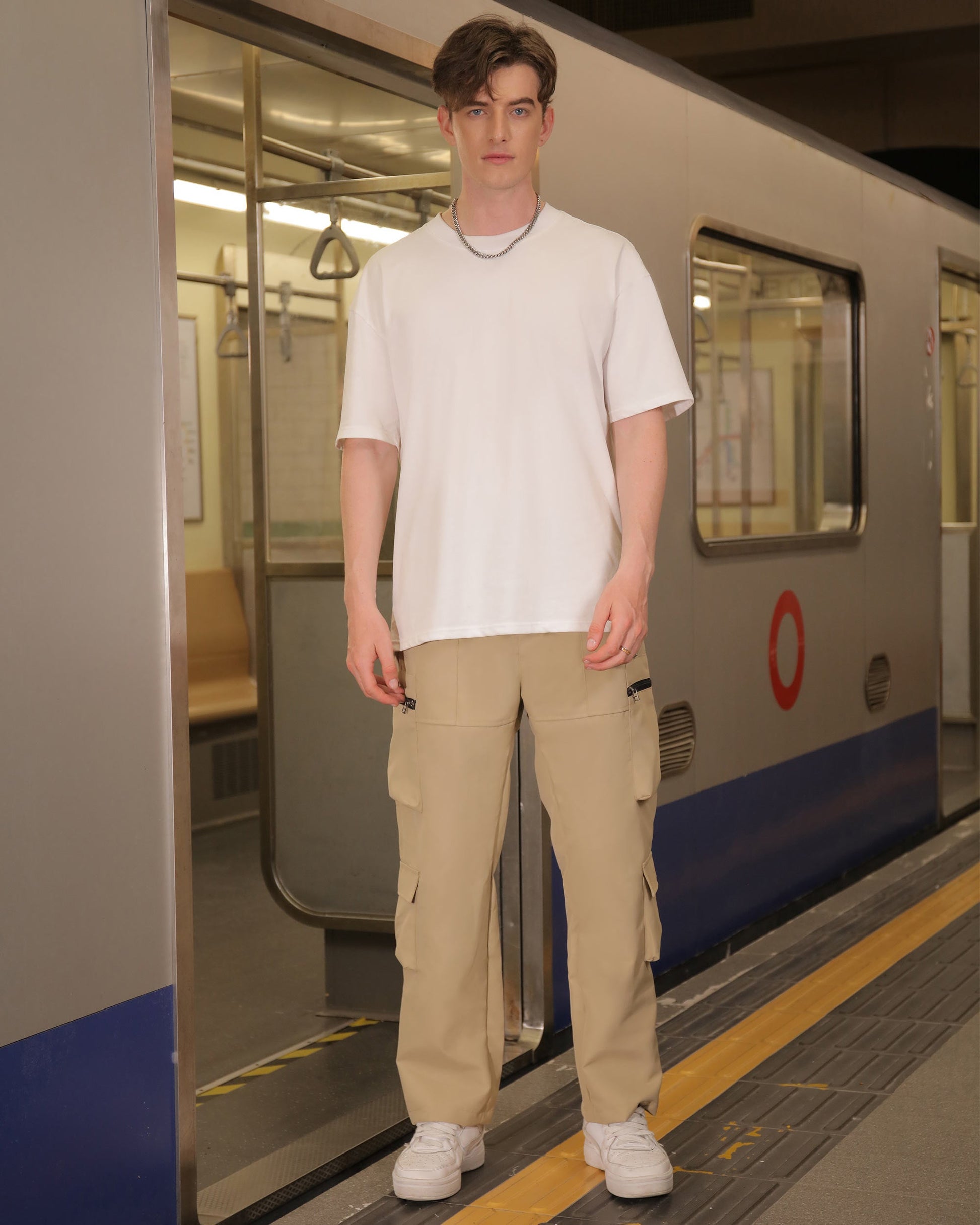 Logeqi stylish cargo pants for men in beige worn with white t-shirt and sneakers at subway station