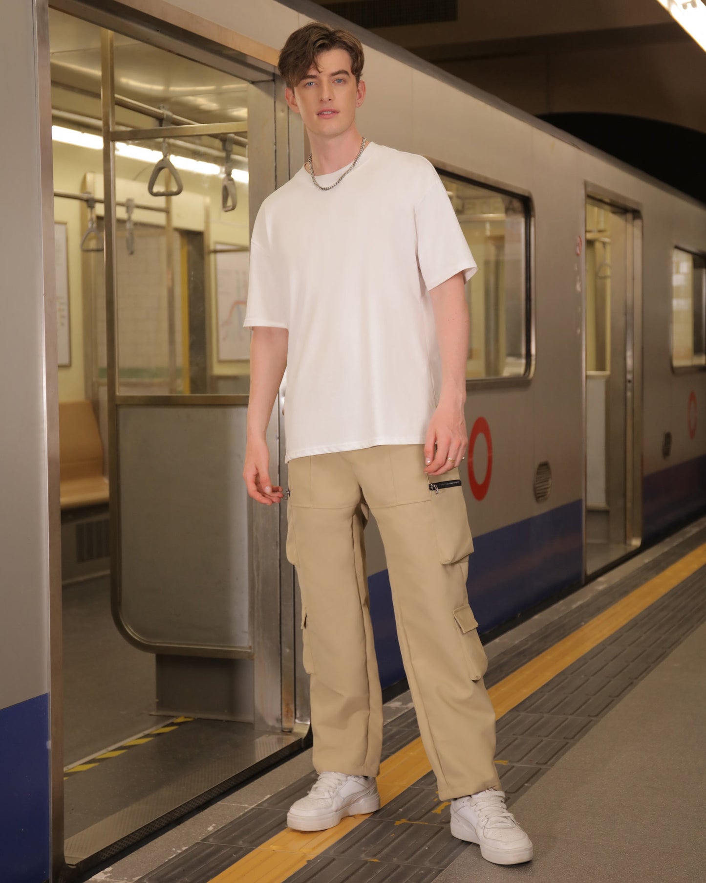 Man wearing Logeqi stylish cargo pants for men in beige with a white t-shirt at a subway station