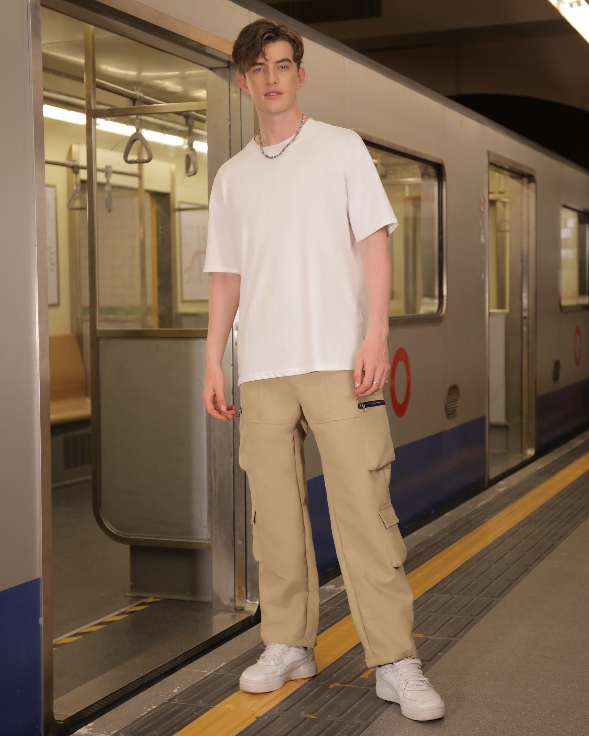 Man wearing Logeqi stylish cargo pants for men in beige with a white t-shirt at a subway station