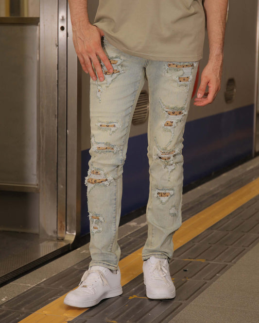 Logeqi distressed ripped blue jeans worn by male model with white sneakers and casual beige shirt