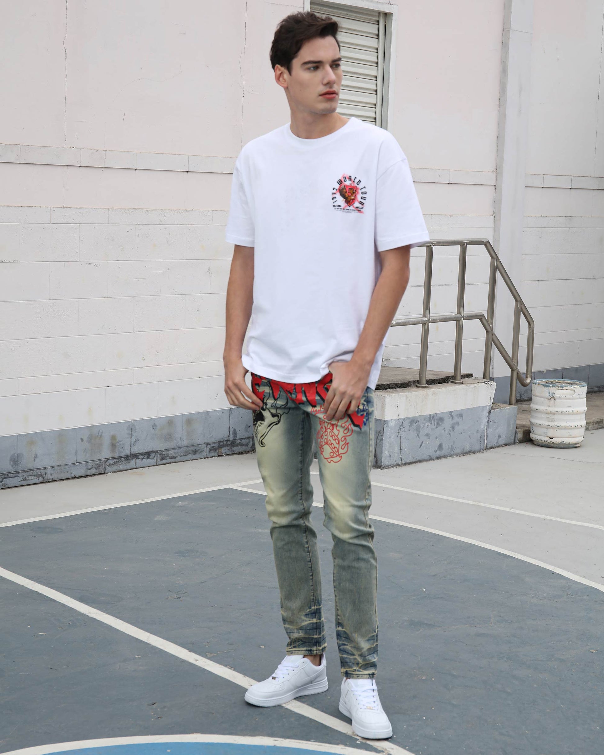 Man wearing Logeqi vintage graffiti jeans with faded washes and red graffiti designs paired with white sneakers
