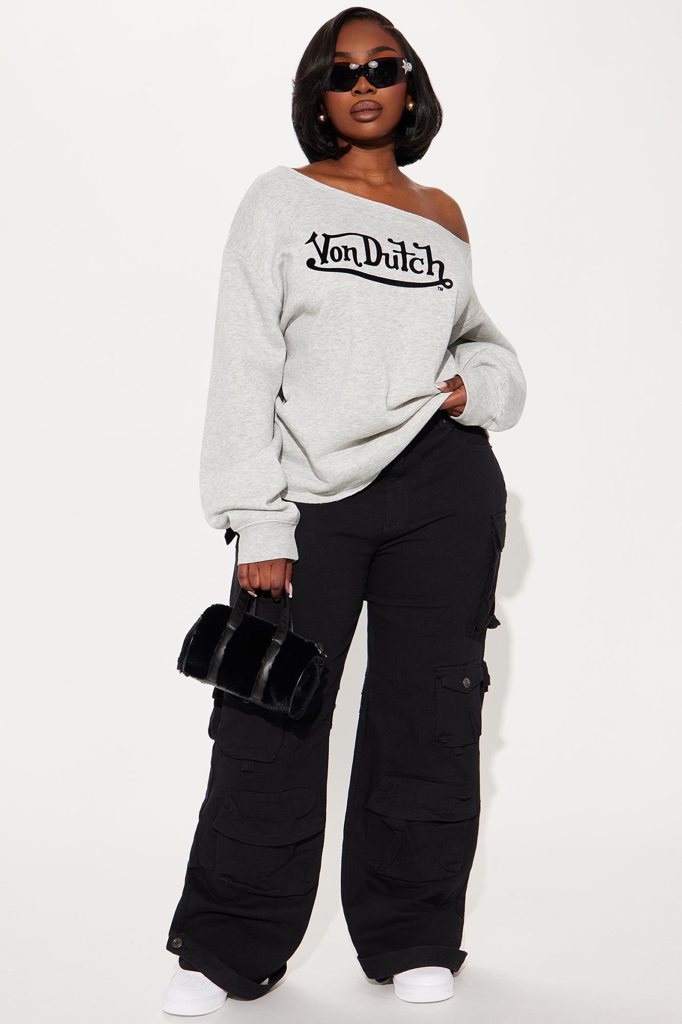 Woman wearing a Von Dutch off shoulder sweatshirt in gray with black cargo pants and sunglasses