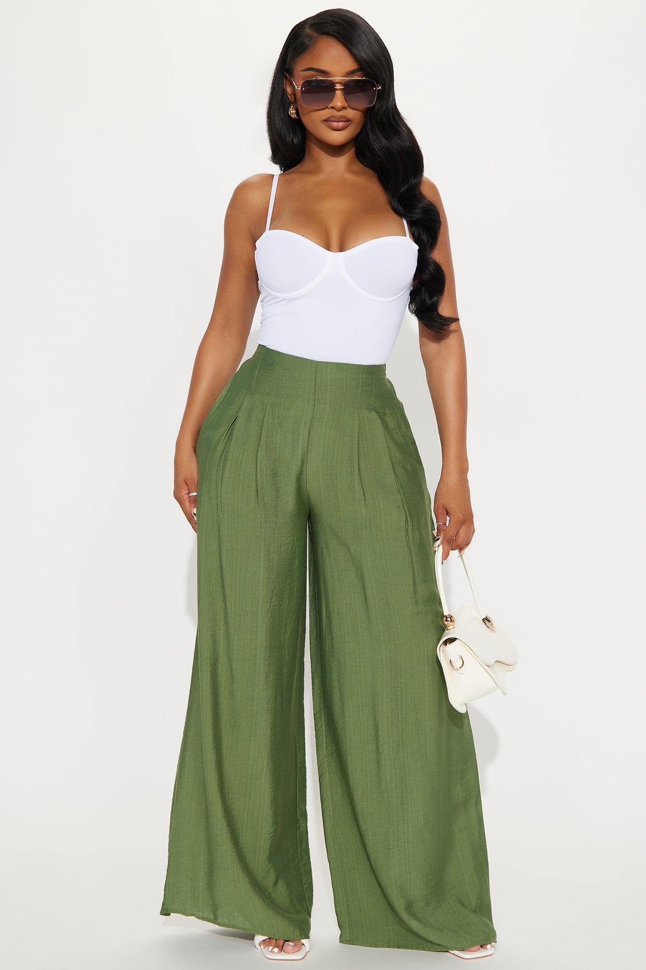 Model wearing a white seamless bodysuit paired with wide-leg olive green pants and sunglasses
