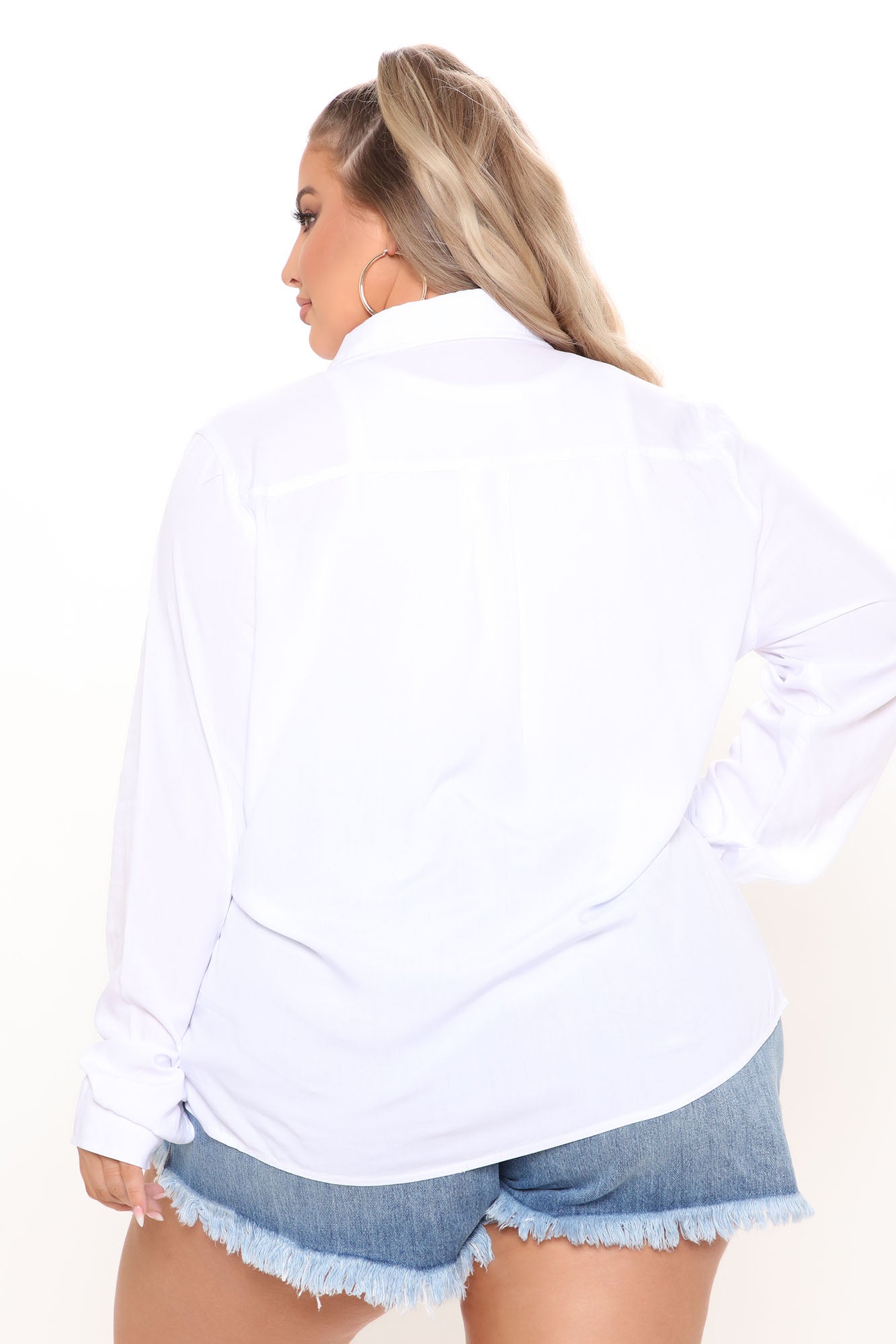 Back view of a woman wearing a white trendy button up shirt for women paired with denim shorts